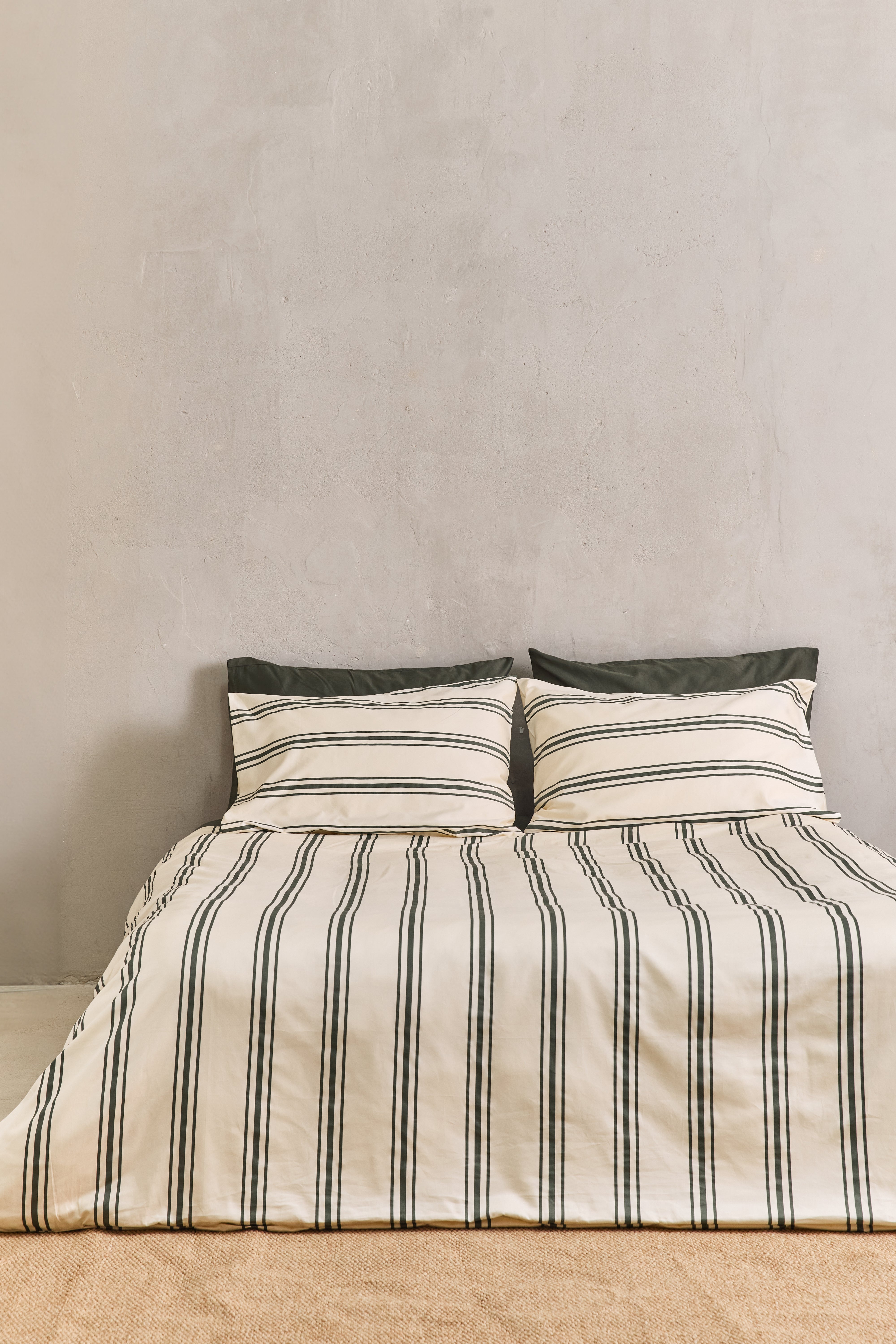 מיטה זוגית עם מצעי כותנה בצבע קרם עם פסים בצבע ירוק זית ושילוב של שתי כריות עם ציפיות בצבע ירוק זית חלק