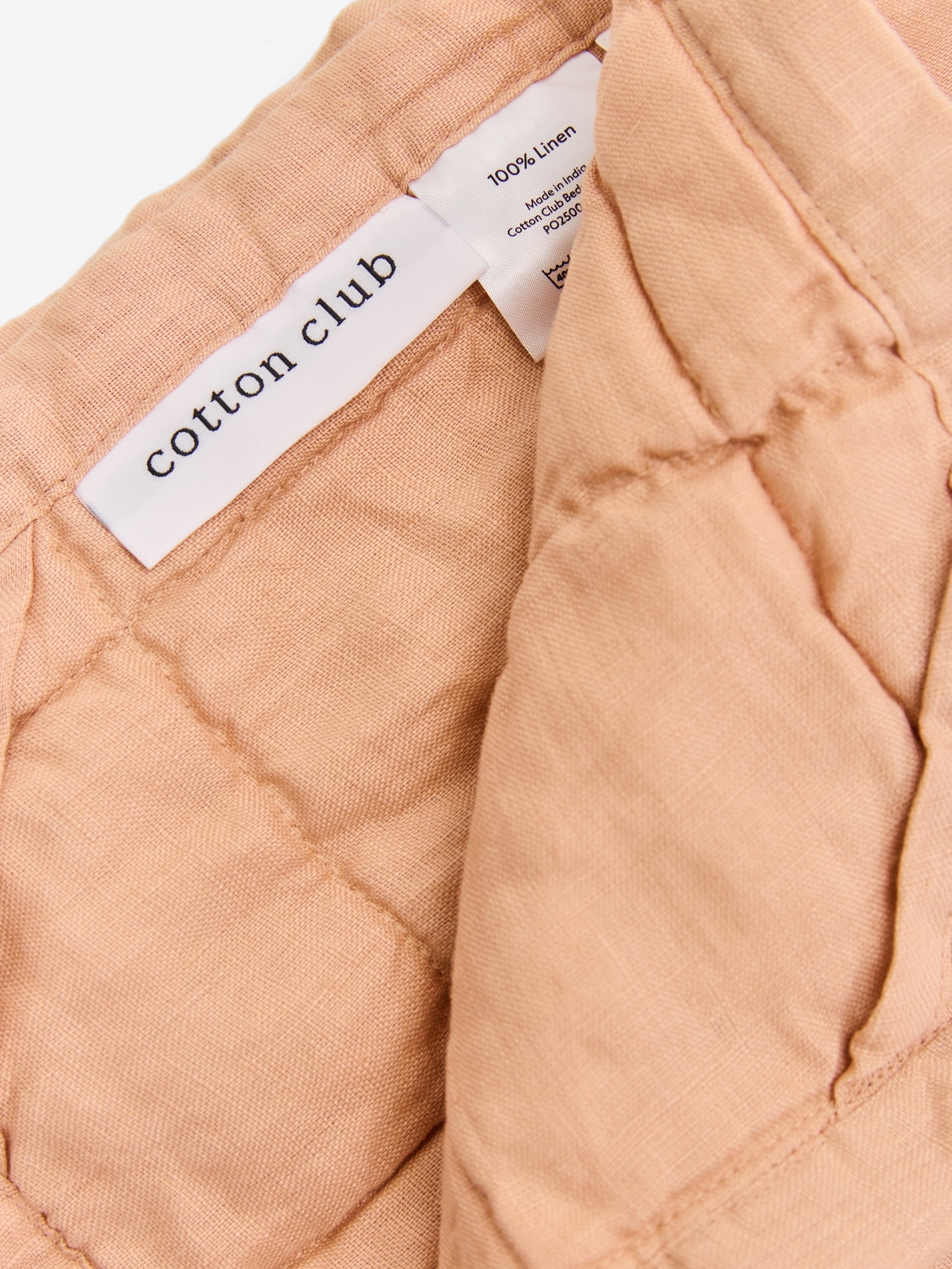 תקריב של שמיכת קווילט מפשתן בצבע ורדרד וטיקט לוגו