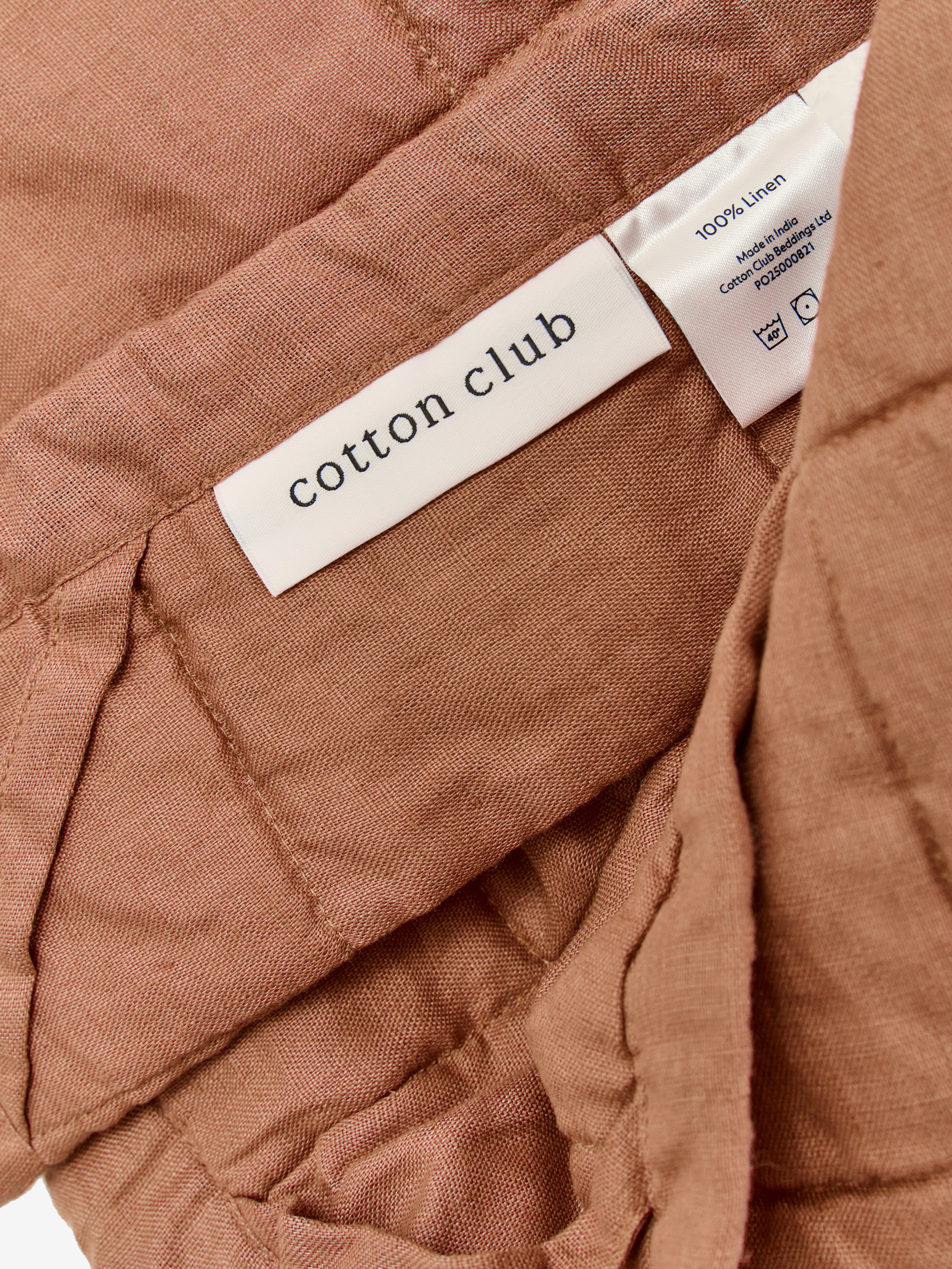 תקריב של שמיכת קווילט מפשתן בצבע מוקה וטיקט לוגו