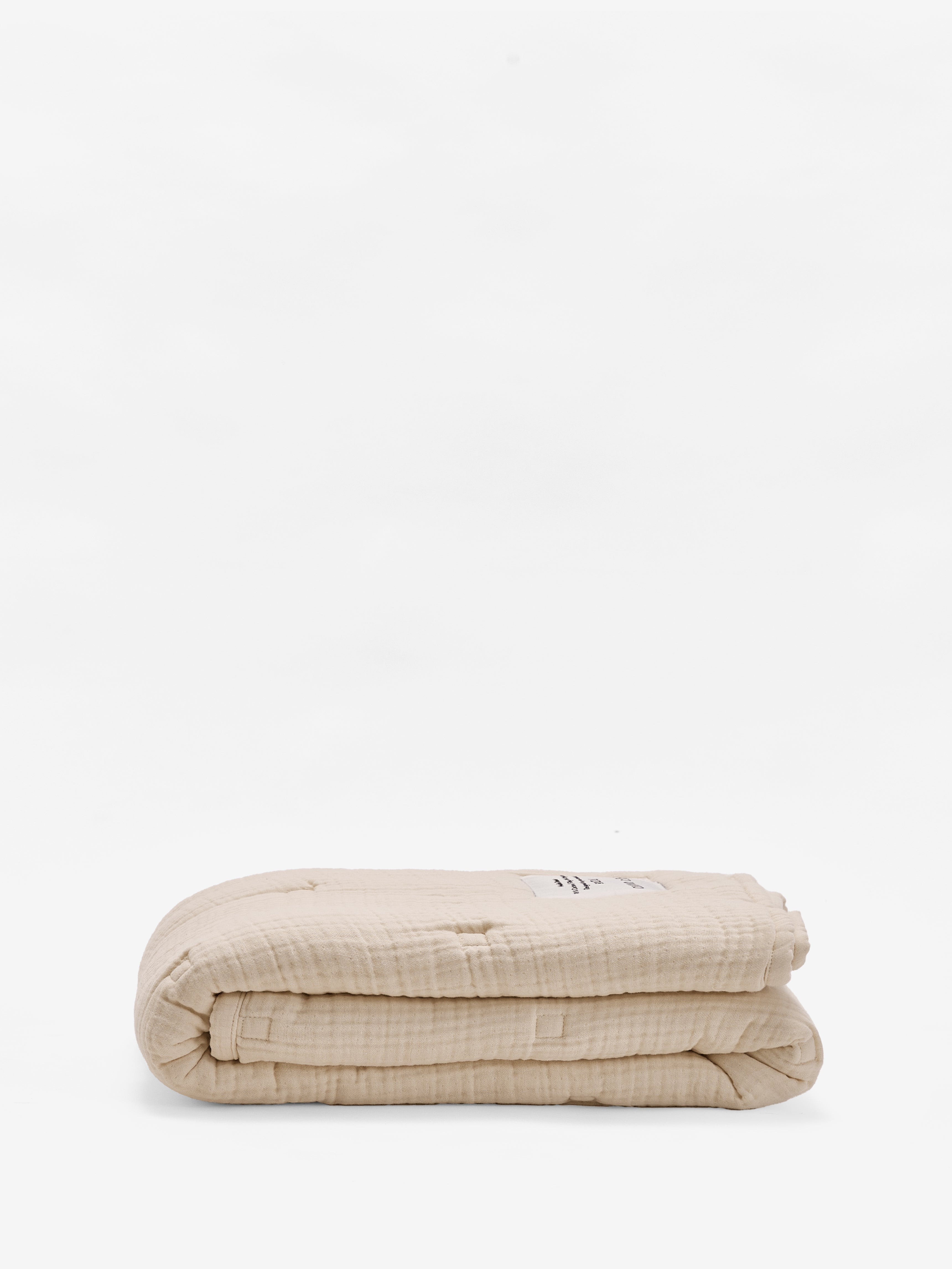 שמיכת פוך מוסלין לתינוקות בצבע קרם מקופלת על רקע לבן