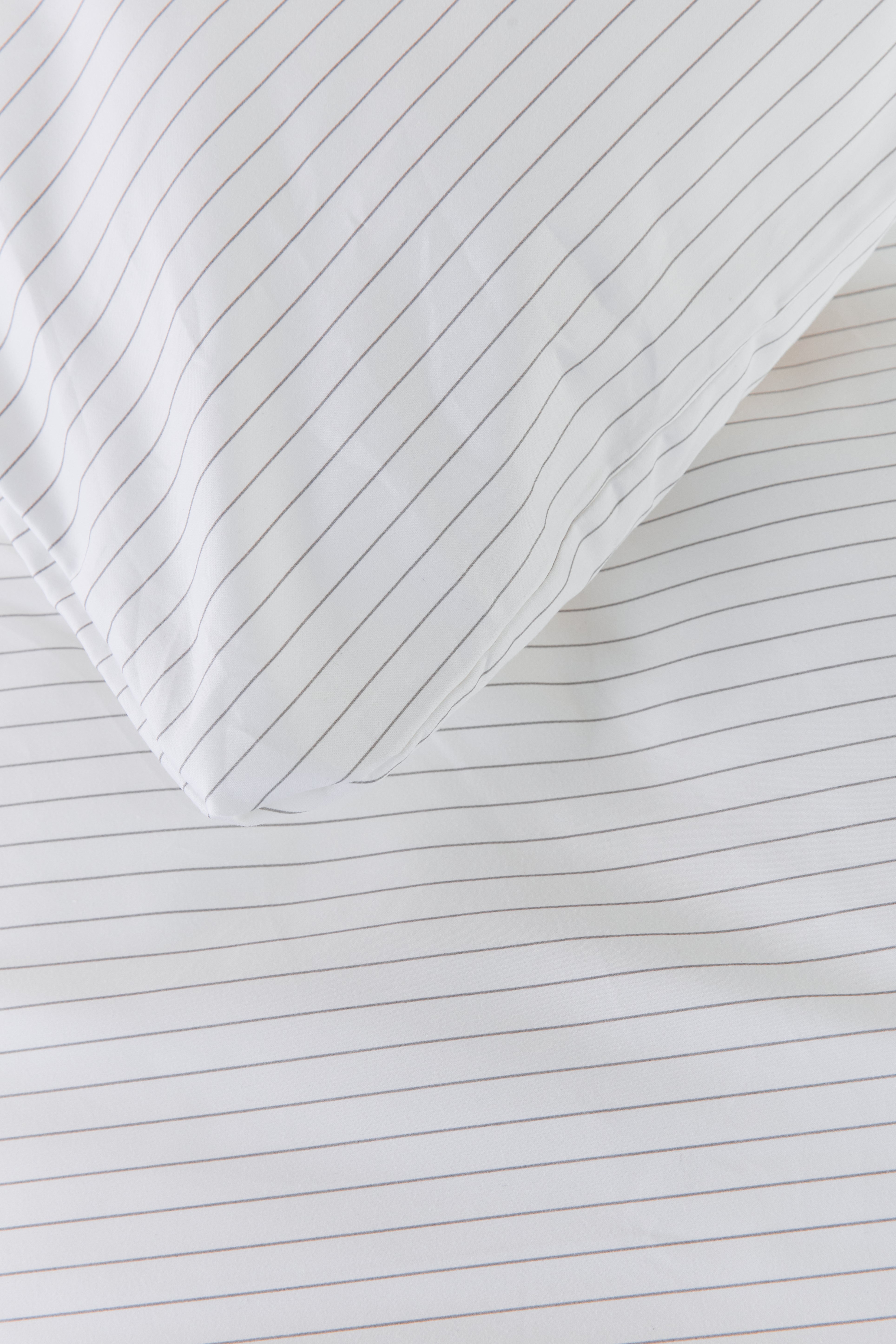 תקריב פינה של כרית עם ציפית כותנה בצבע לבן עם פסים אפורים דקים על שמיכה עם ציפה זהה