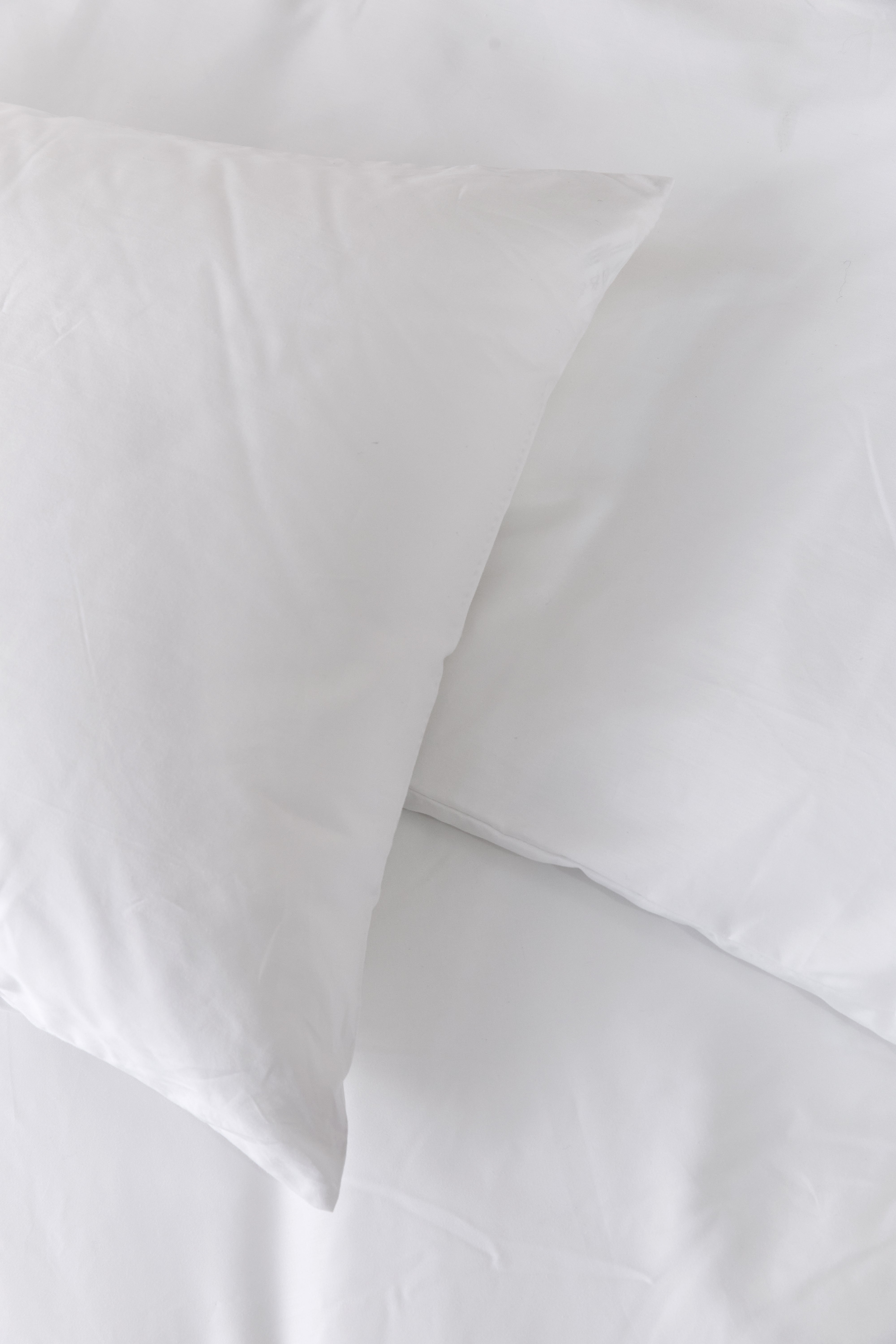 כרית מונחת על שמיכה עם מצעי כותנה לבנים