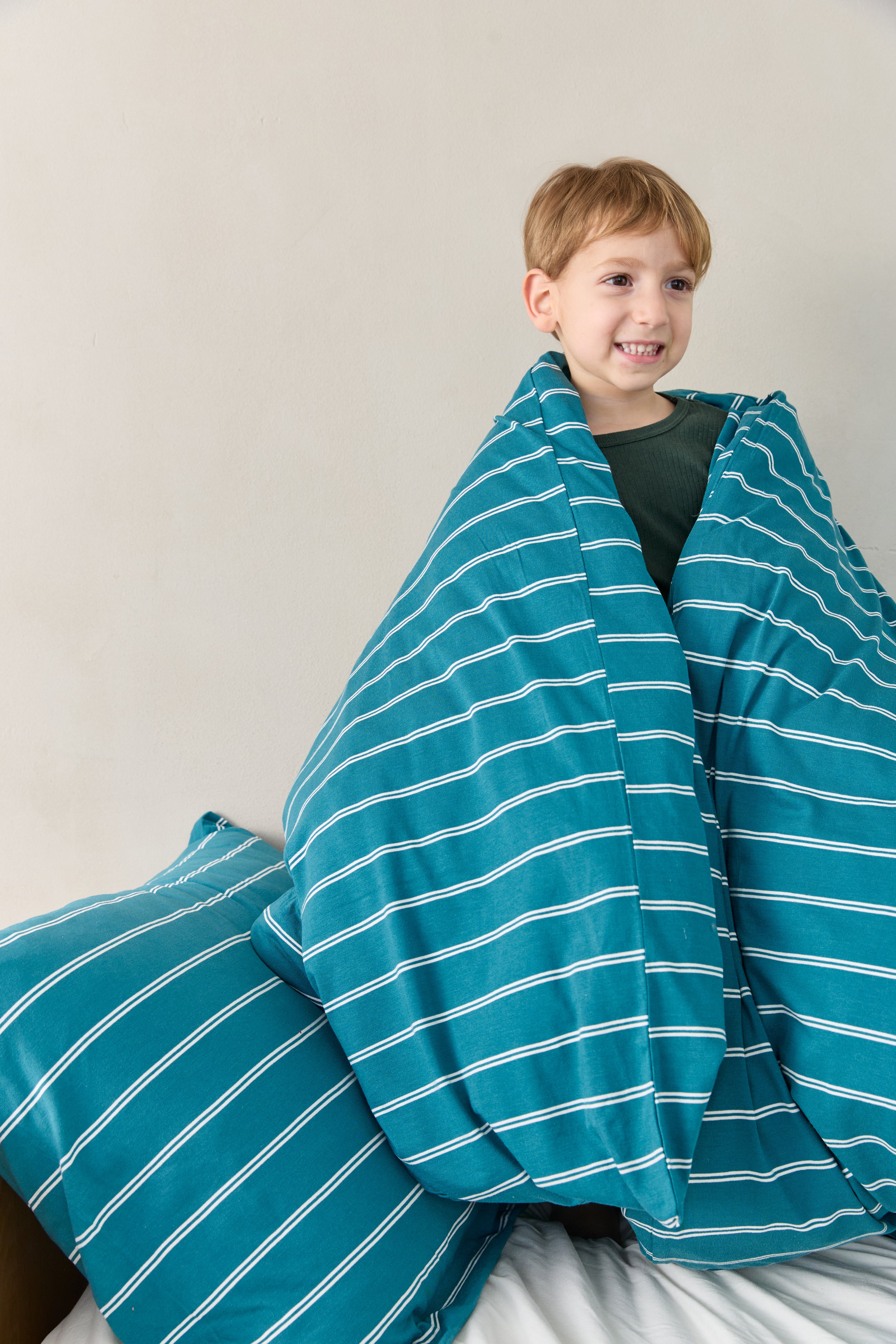 ילד מתעטף בשמיכת פוך עם מצעי ג'רסי במבוק בצבע טורקיז עם פסים לבנים
