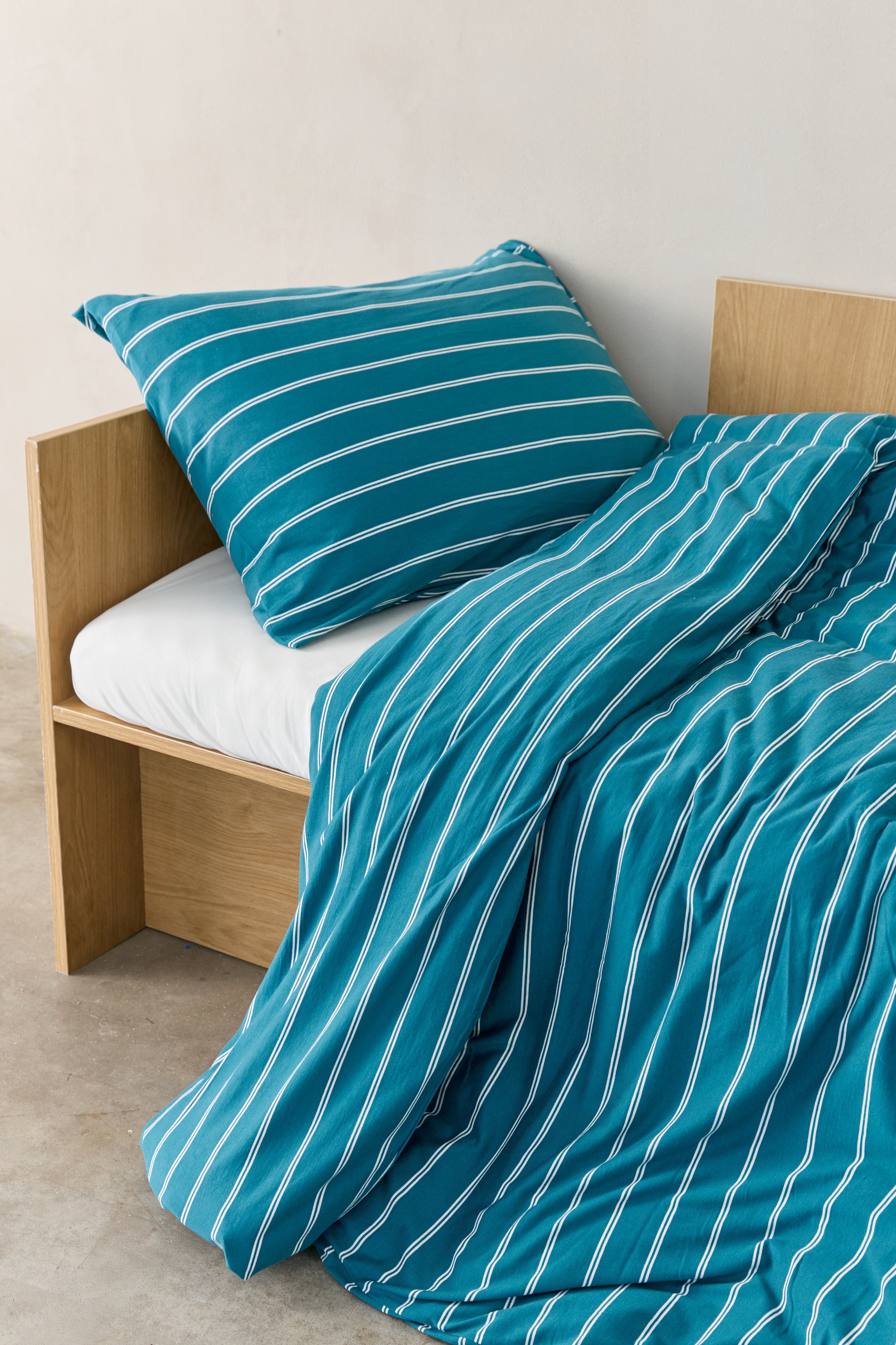 תקריב מיטת ילדים עם מצעי ג'רסי במבוק בצבע טורקיז עם פסים לבנים, הסדין לבן חלק