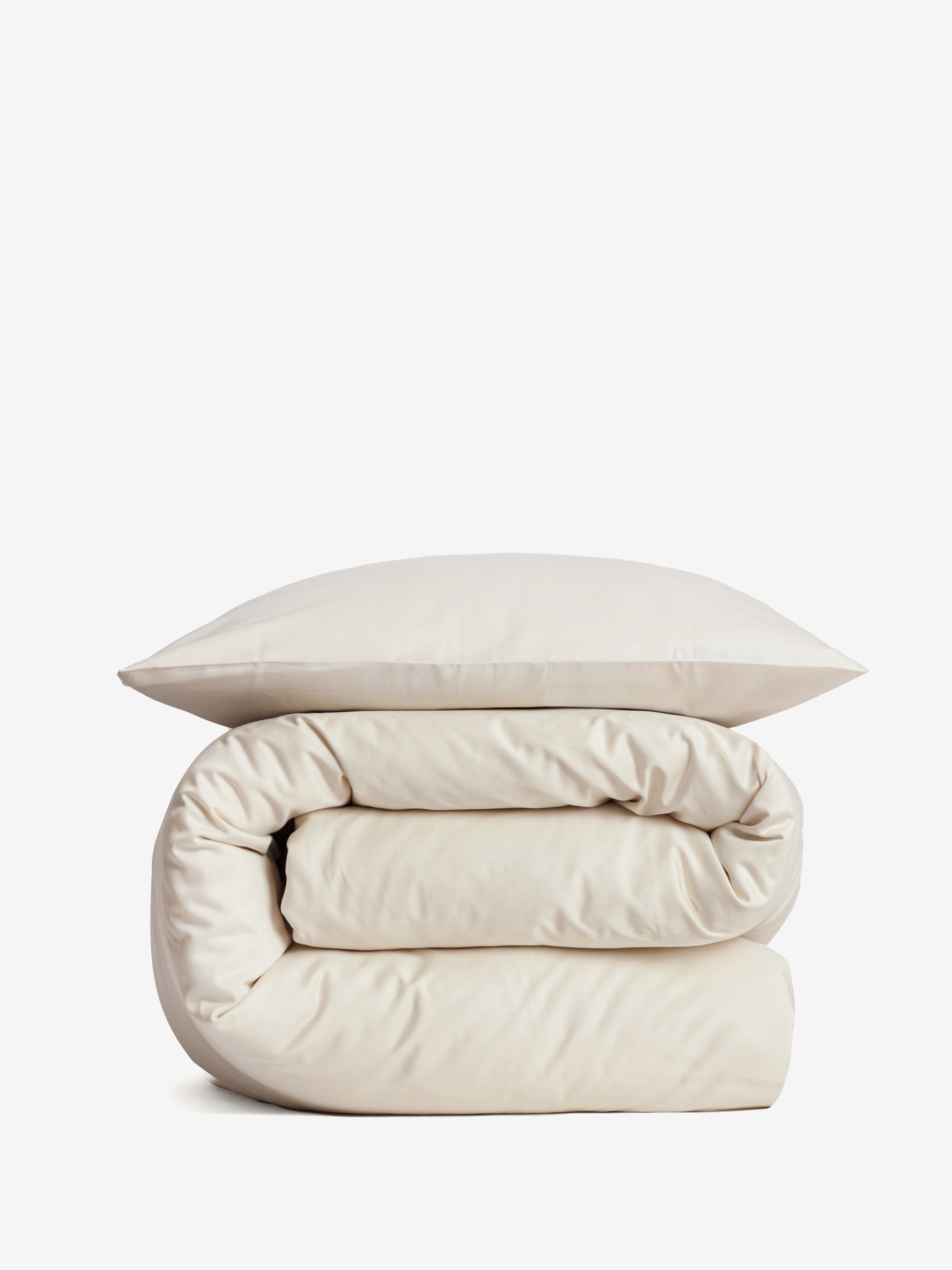 סט מצעי כותנה בצבע קרם, שמיכה מגולגלת וכרית מעליה