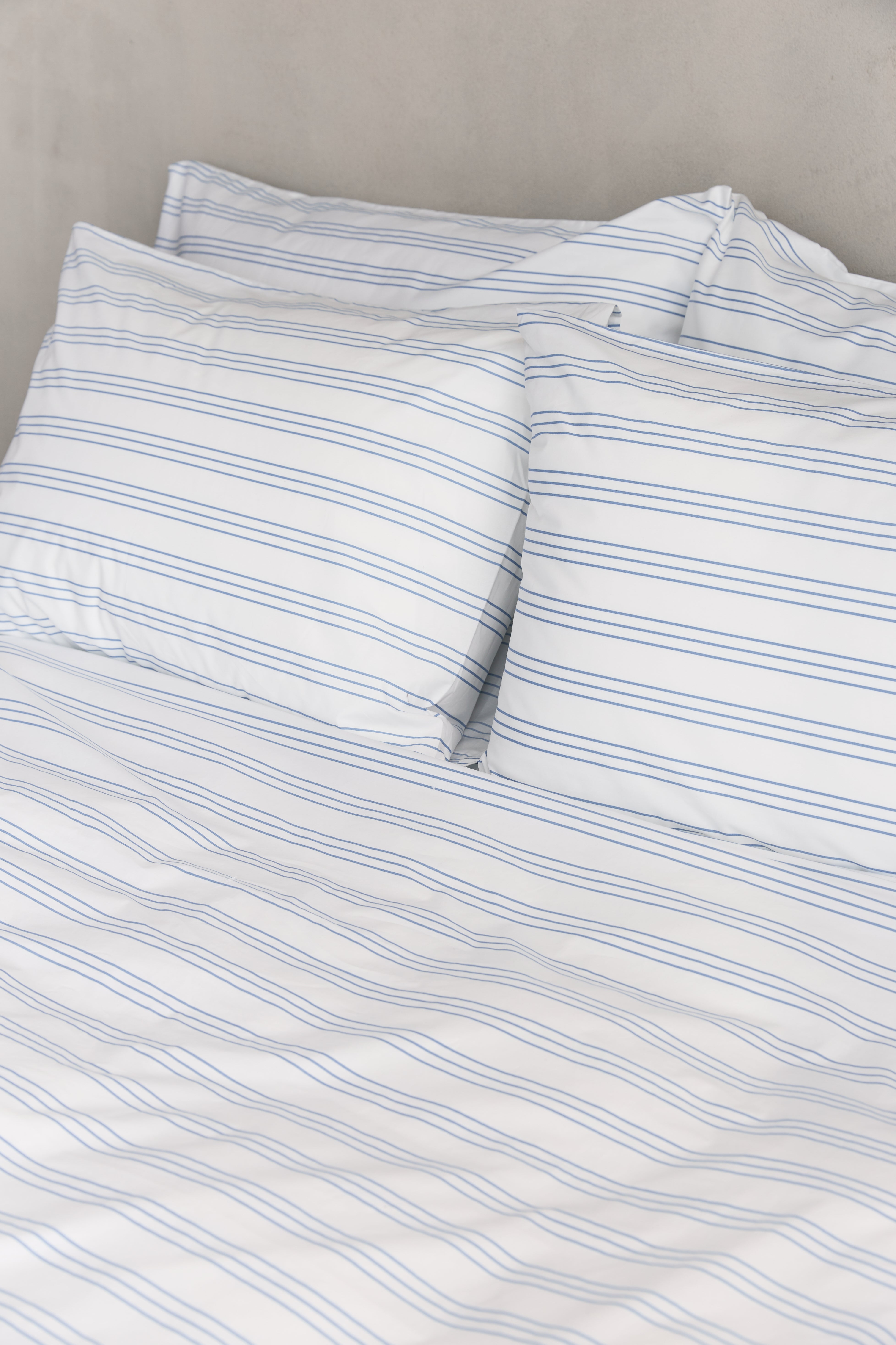 תקריב מיטה זוגית עם סט מצעי כותנה לבנים עם פסים לרוחב בצבע תכלת