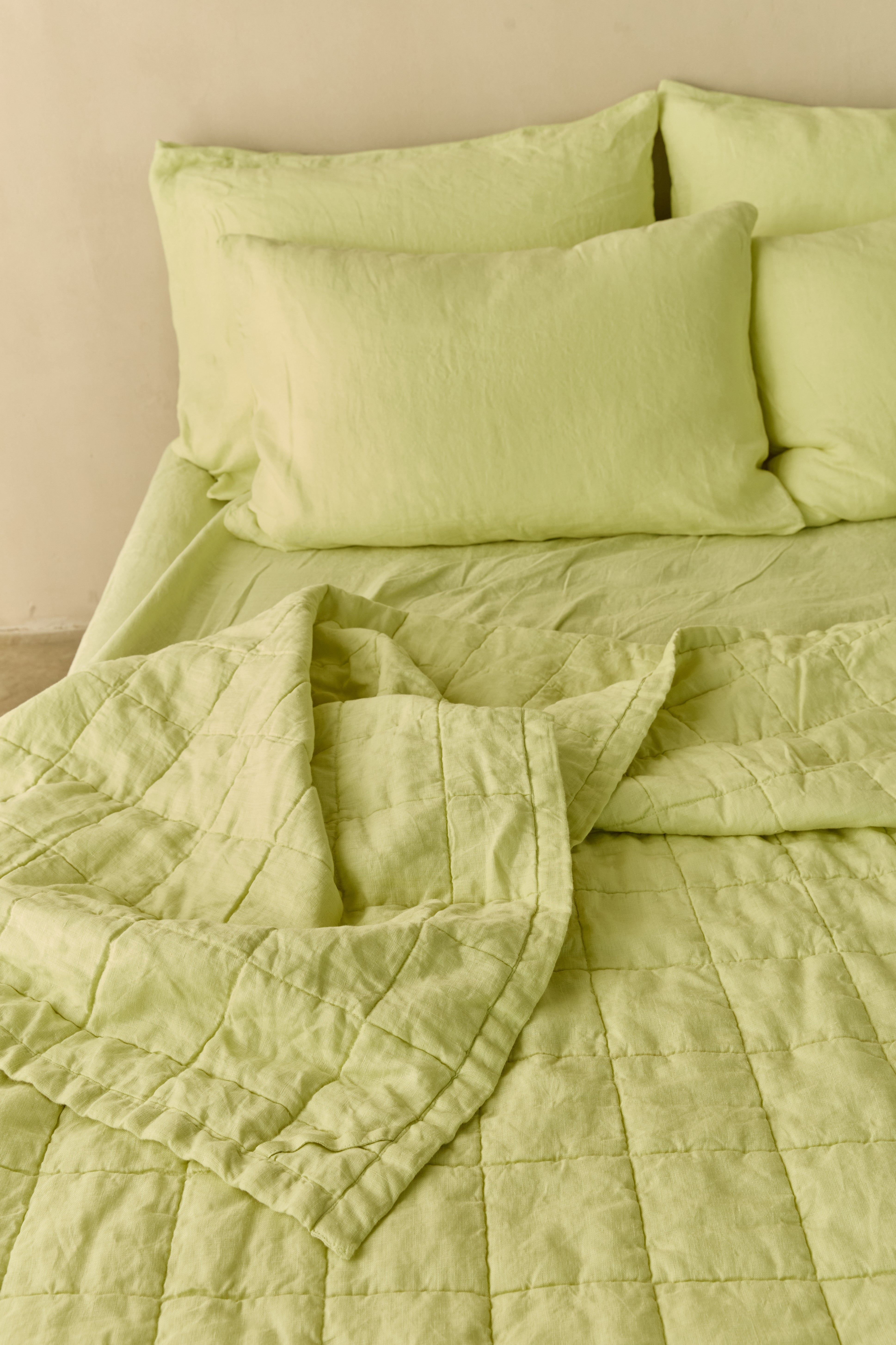 מיטה זוגית עם מצעי פשתן בצבע ליים ועליה שמיכת פשתן קווילט בצבע תואם