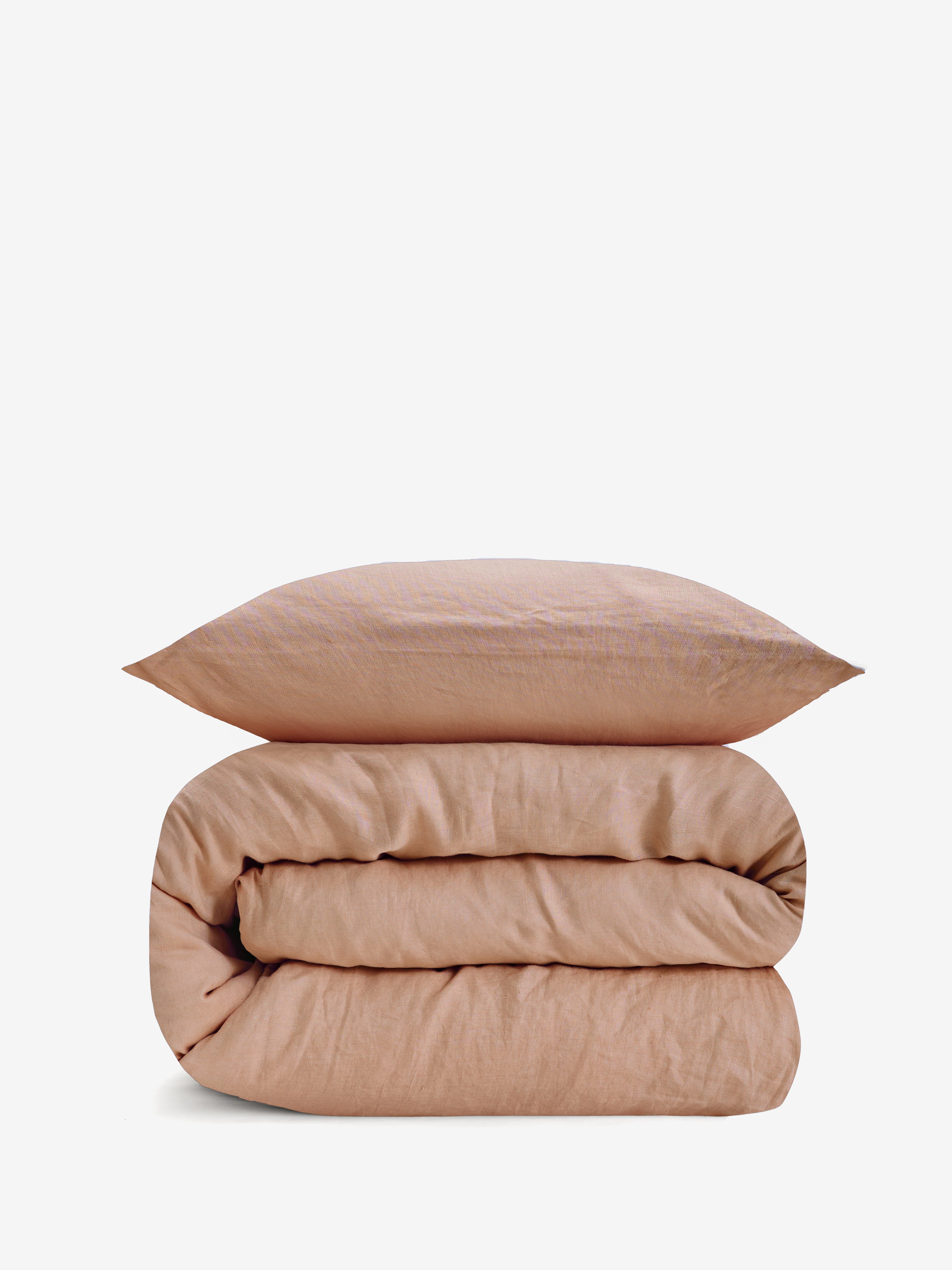 סט מצעי פשתן  בצבע ורדרד, שמיכה מגולגלת וכרית מעליה