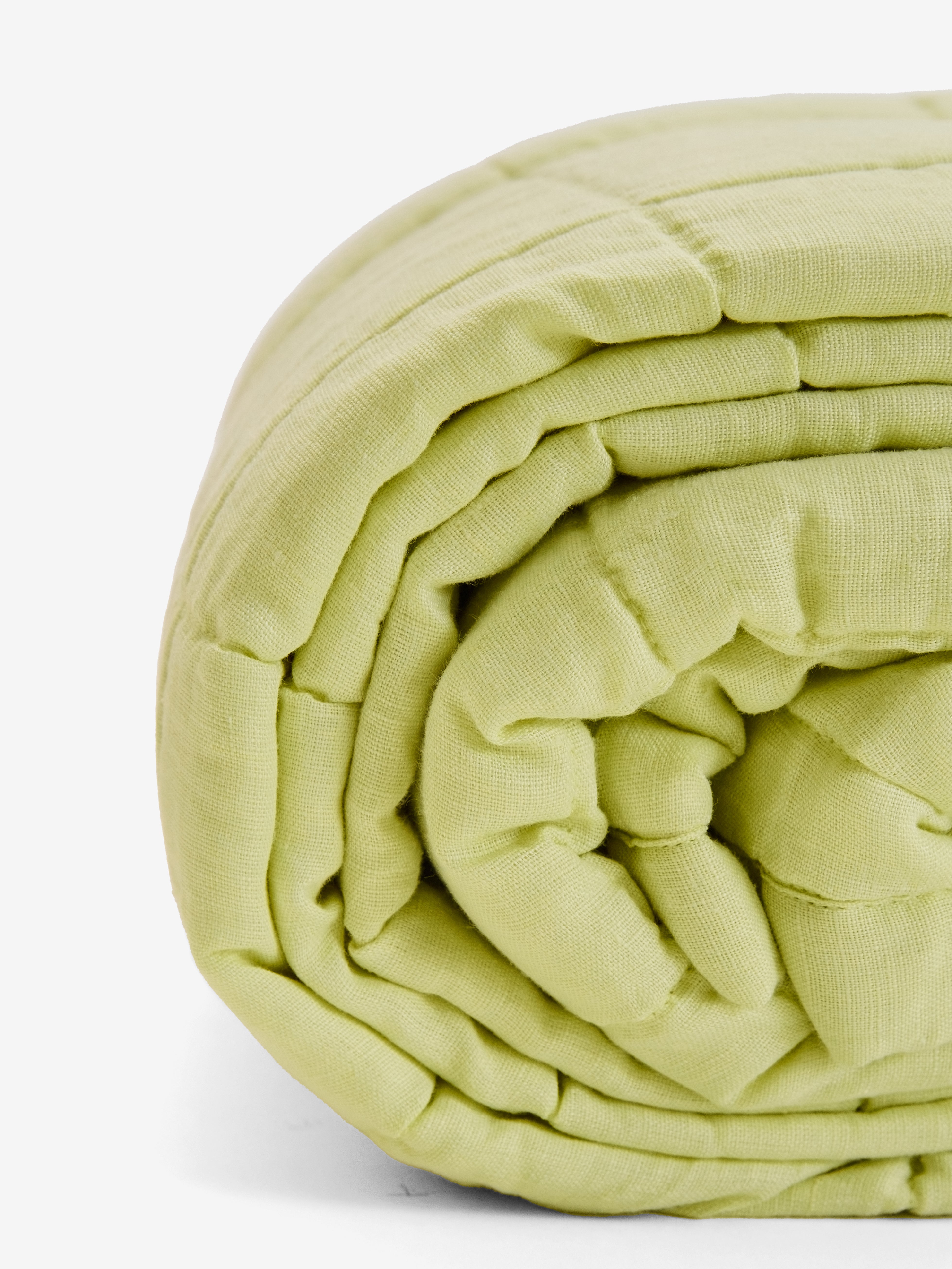 תקריב של שמיכת קווילט מפשתן בצבע ליים מגולגלת על רקע לבן