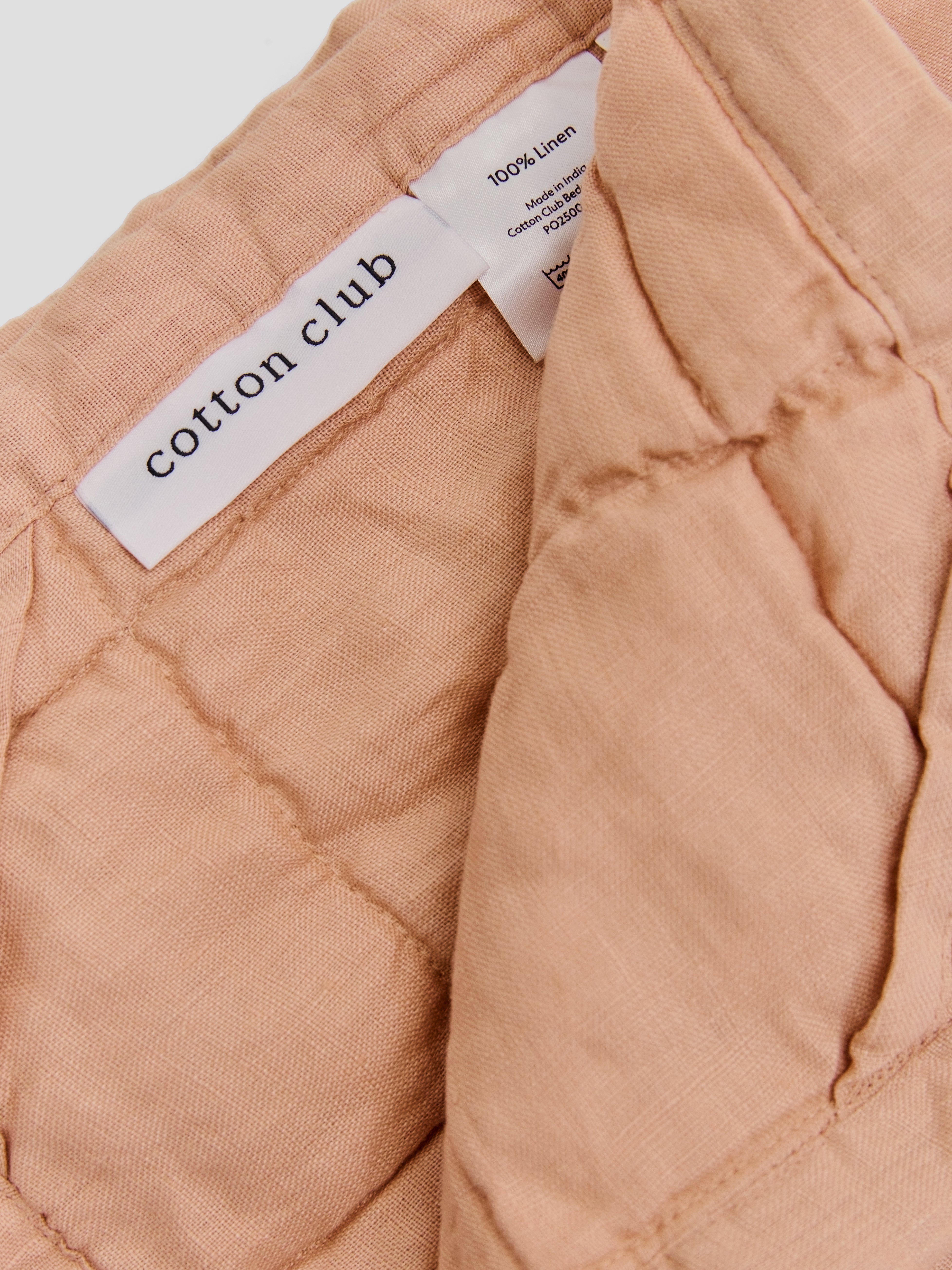 תקריב של שמיכת קווילט מפשתן בצבע ורדרד וטיקט לוגו 