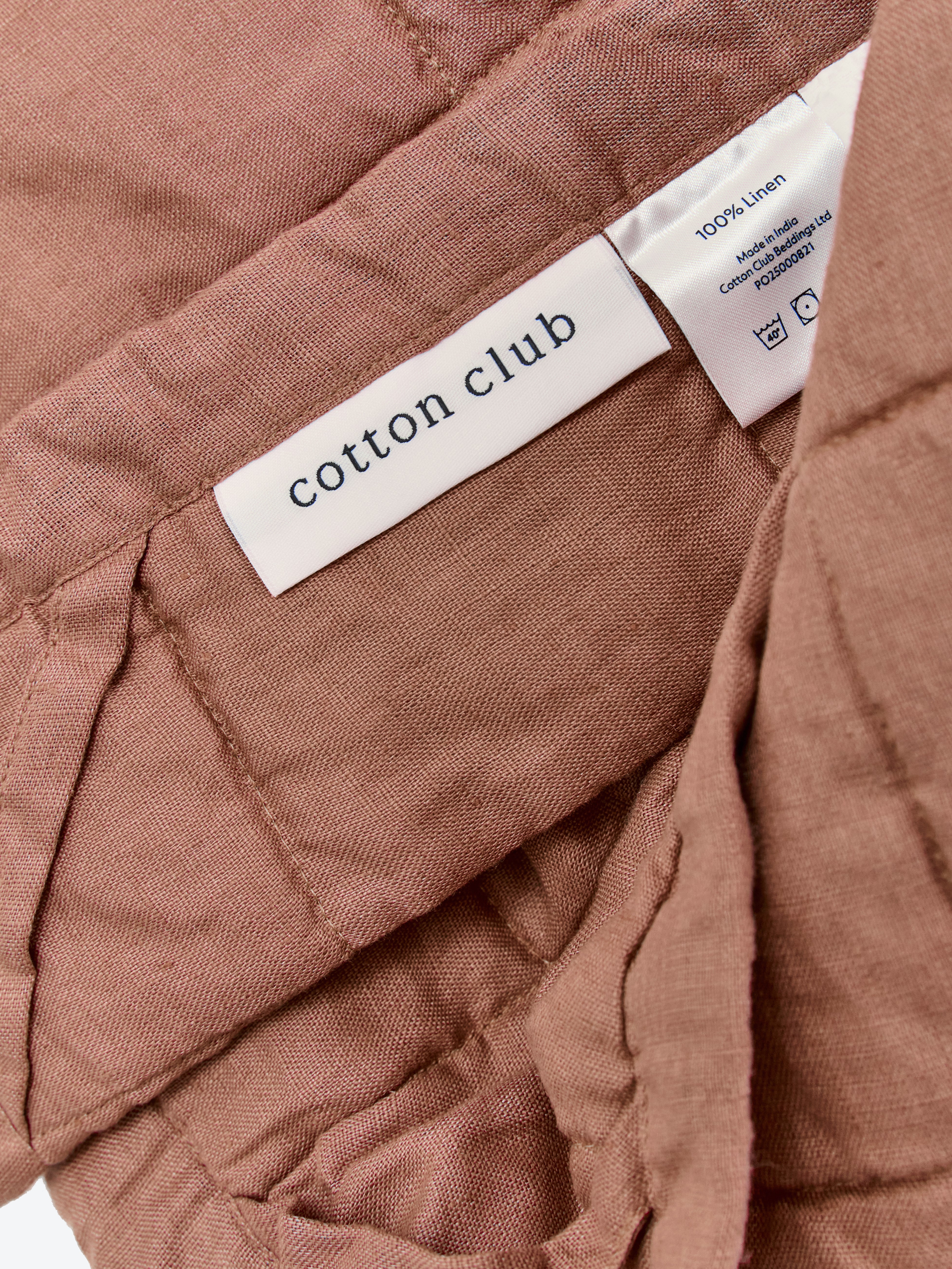 תקריב של שמיכת קווילט מפשתן בצבע מוקה וטיקט לוגו 