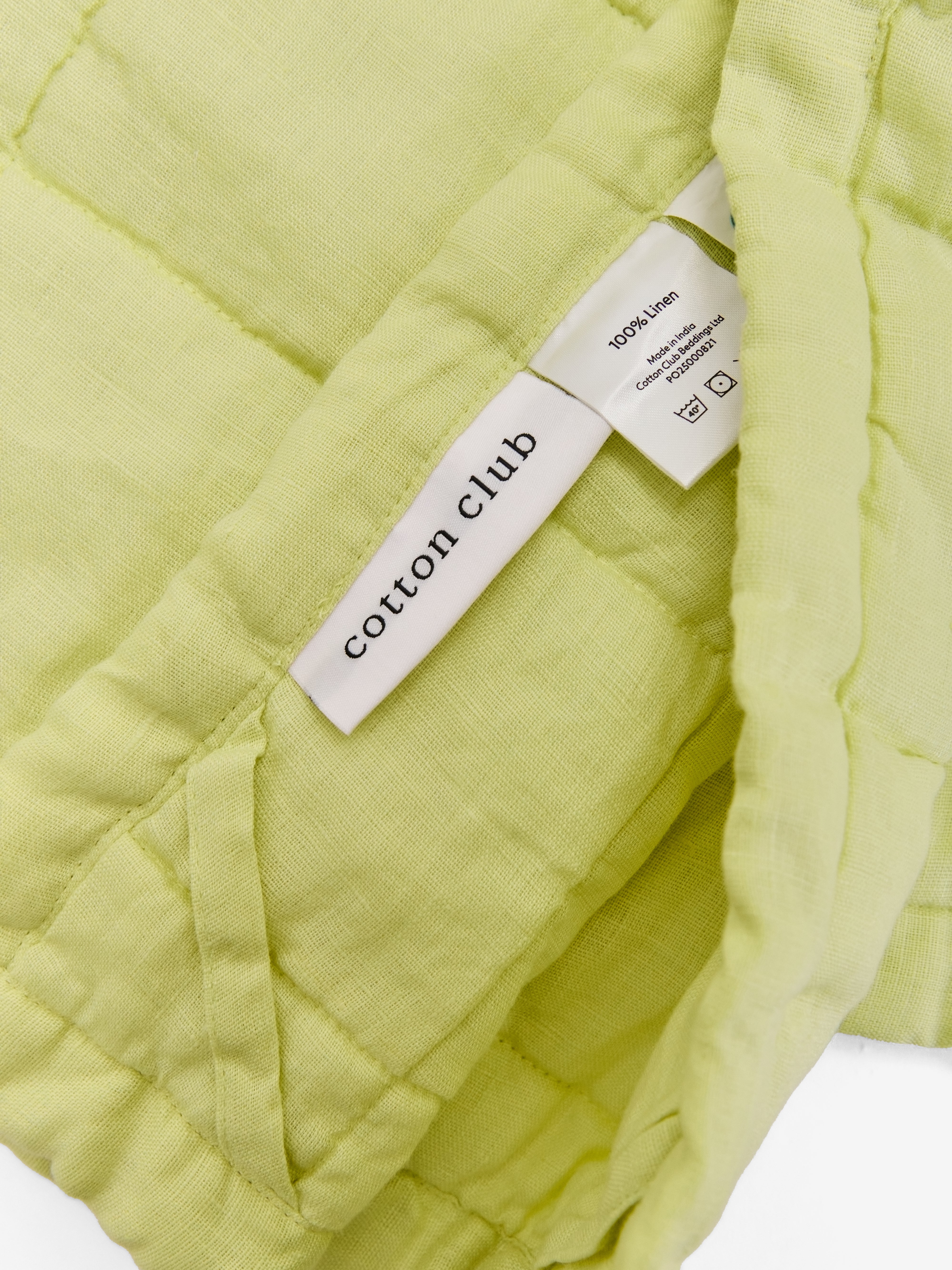 תקריב של שמיכת קווילט מפשתן בצבע ליים וטיקט לוגו 