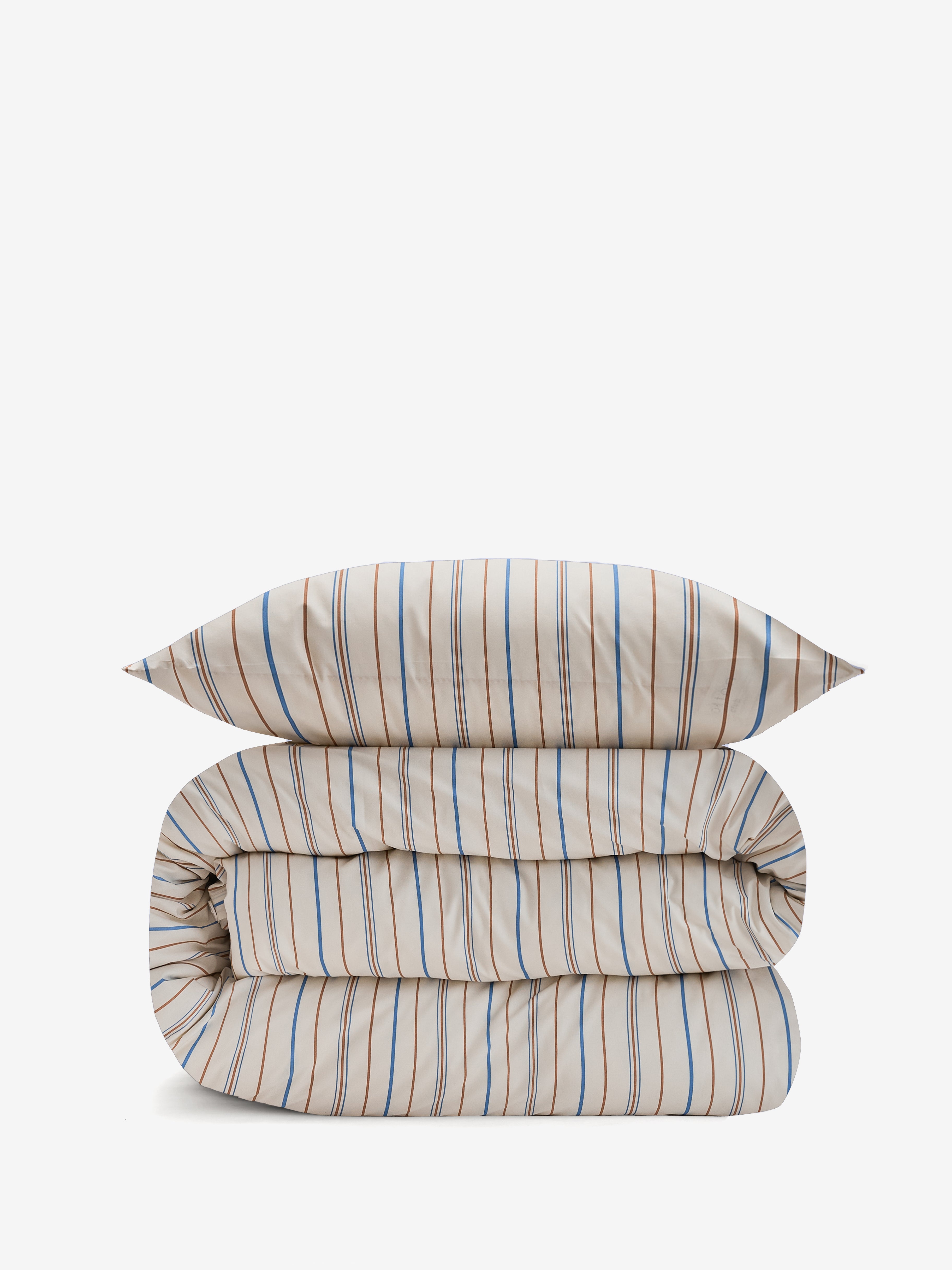 שמיכה מגולגלת ועליה כרית עם סט מצעי פרקל בצבע קרם עם פסים חומים וכחולים