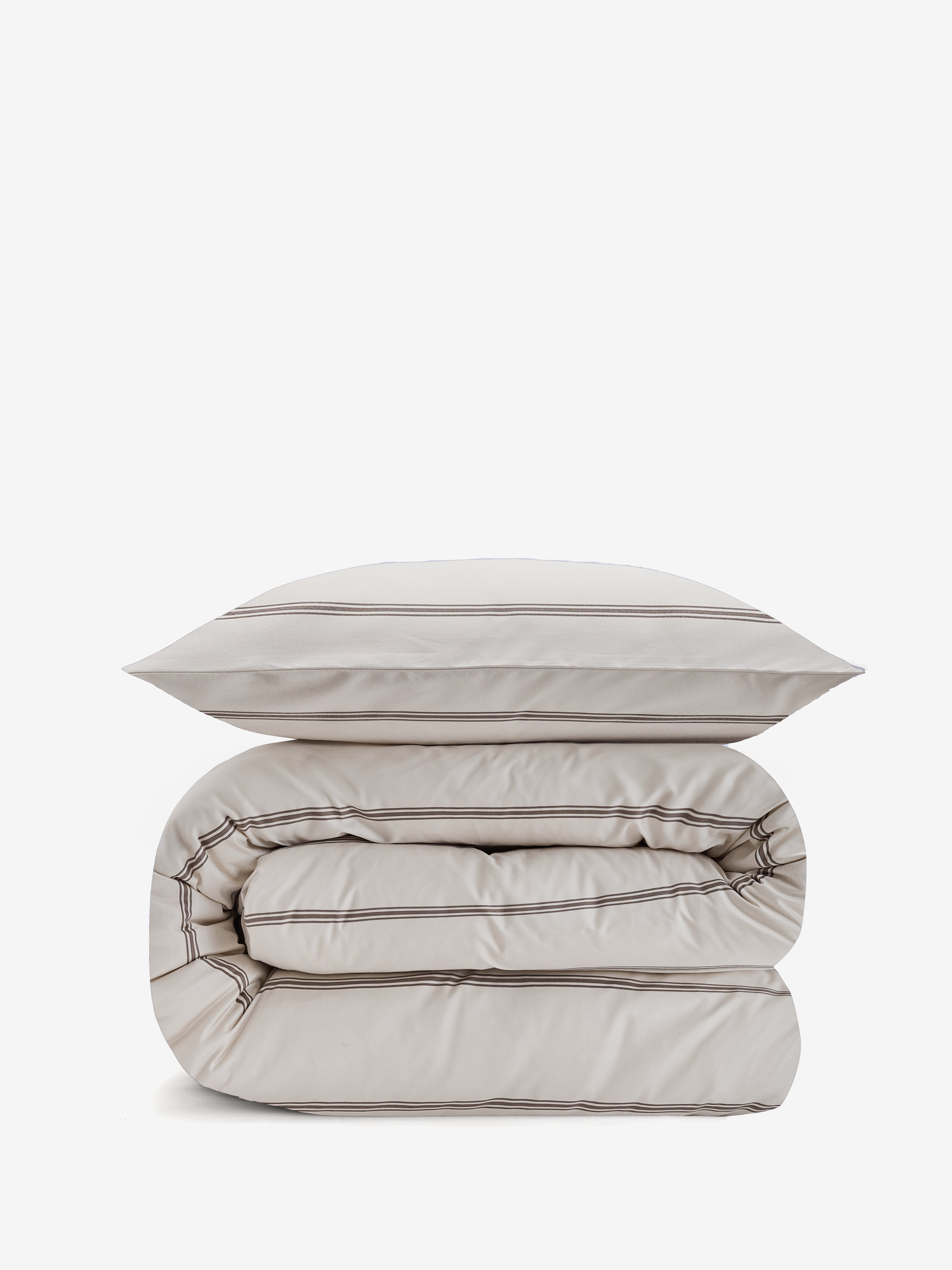 שמיכה מגולגלת ועליה כרית עם מצעי סאטן 500 בצבע קרם עם פסים בצבע אבן