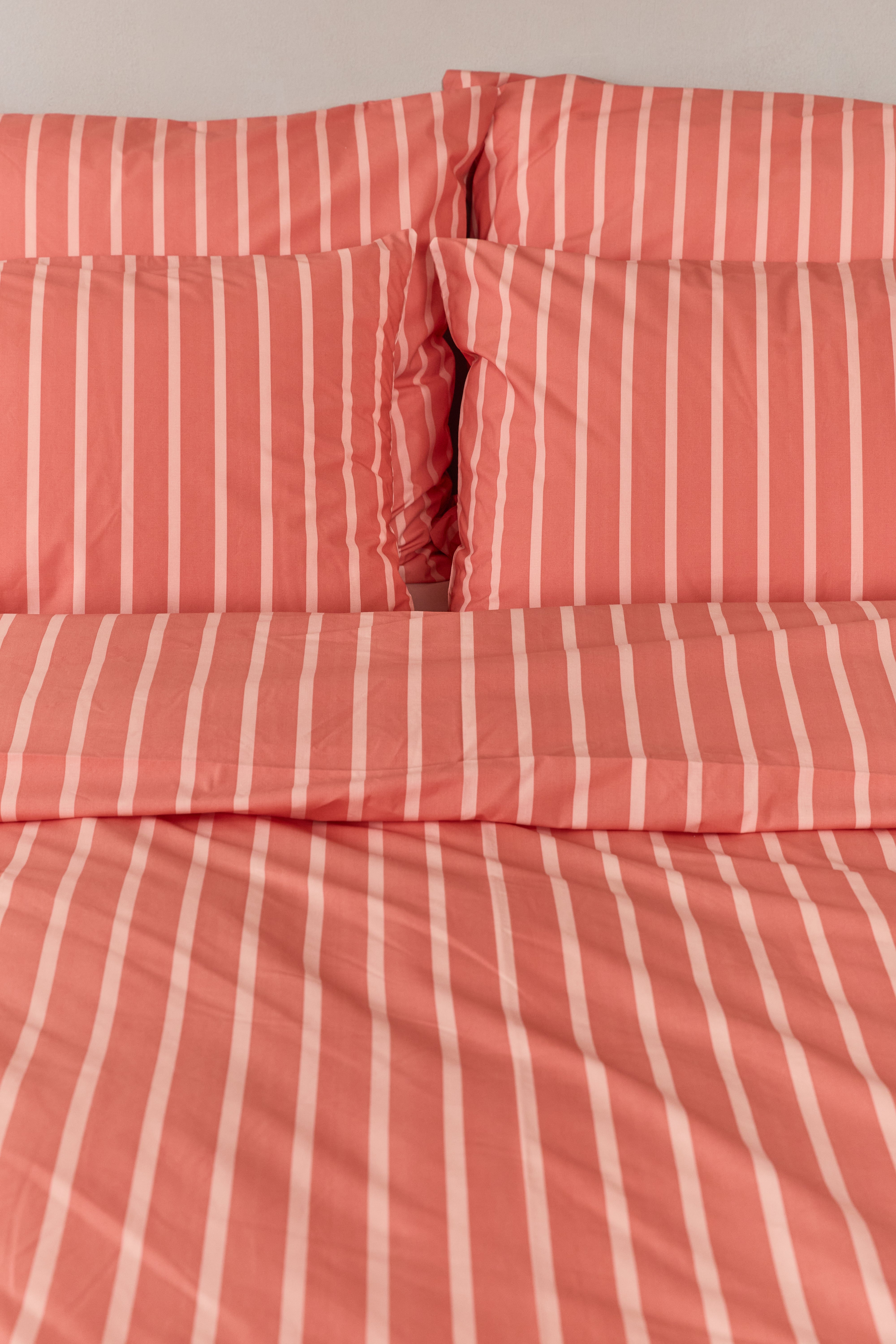 תקריב מיטה זוגית עם מצעי כותנה בצבע אפרסק כהה עם פסים בצבע אפרסק בהיר