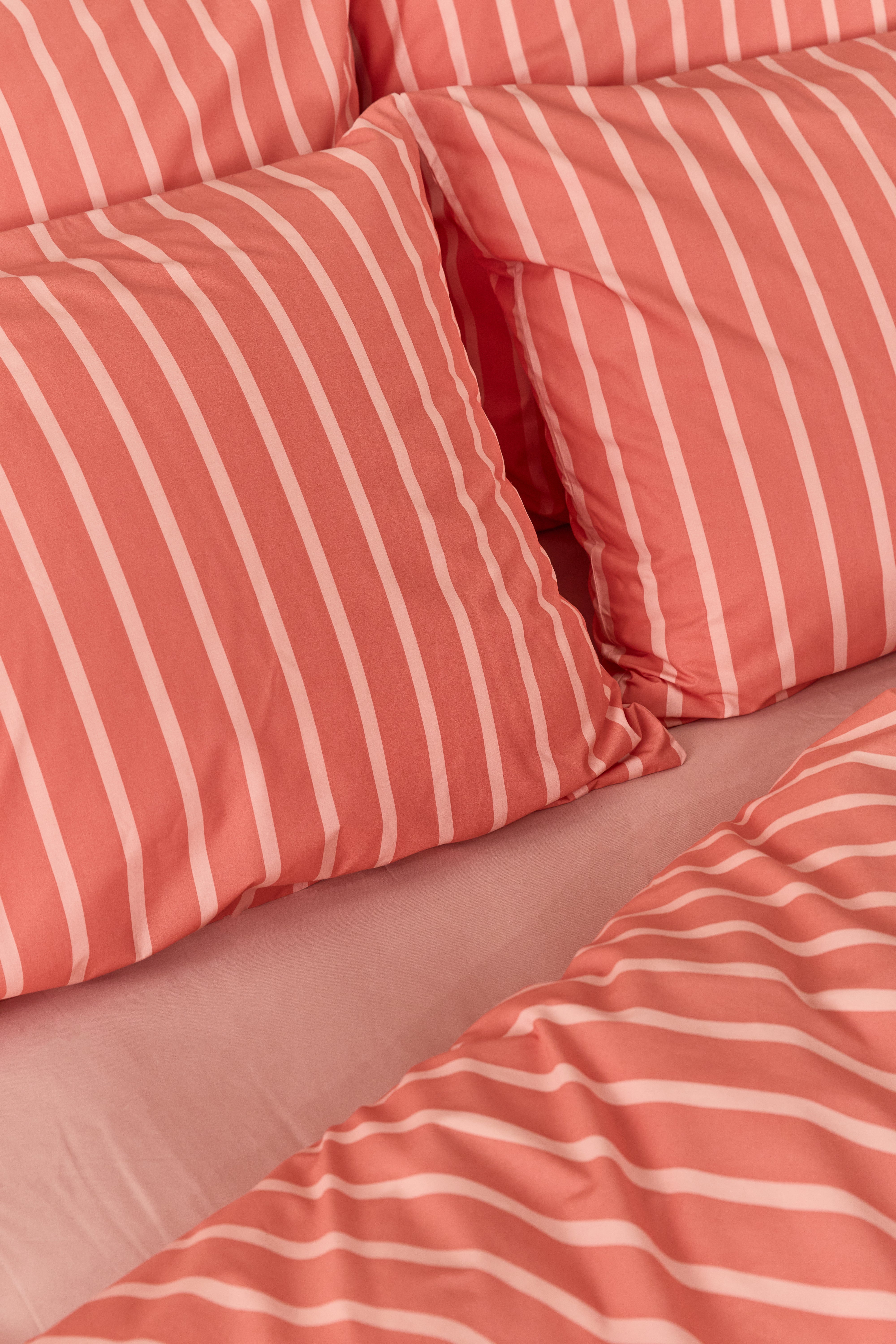 תקריב מיטה זוגית עם סט מצעי כותנה בצבע אפרסק כהה עם פסים של אפרסק בהיר עם סדין חלק בצבע אפרסק בהיר 