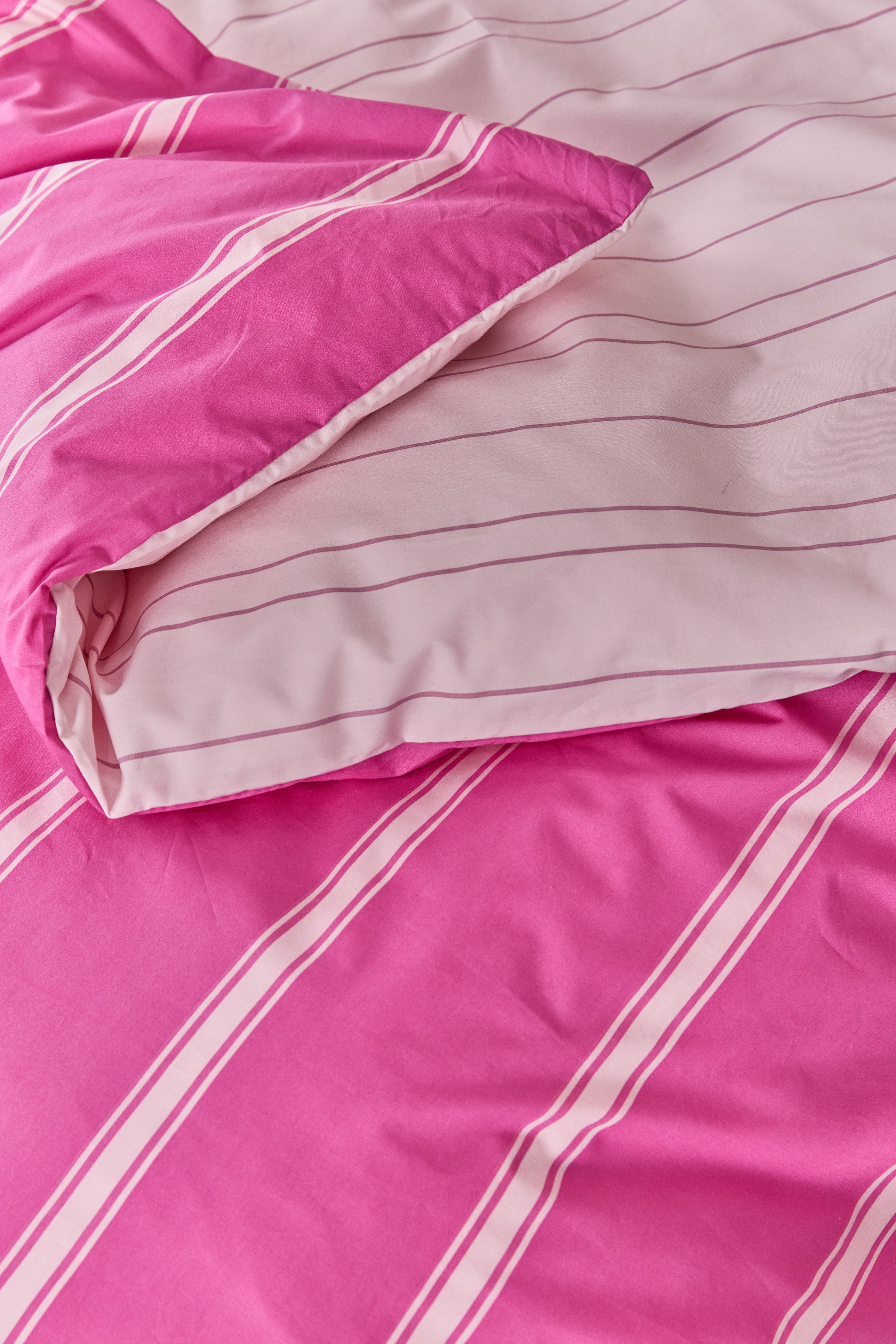 תקריב של שמיכה מקופלת עם הציפה הדו צדדית שרואים את שני הצבעים. צד אחד ורוד פוקסיה עם פסים ורוד בהיר וצד שני ורוד בהיר עם פסים ורוד כהה.