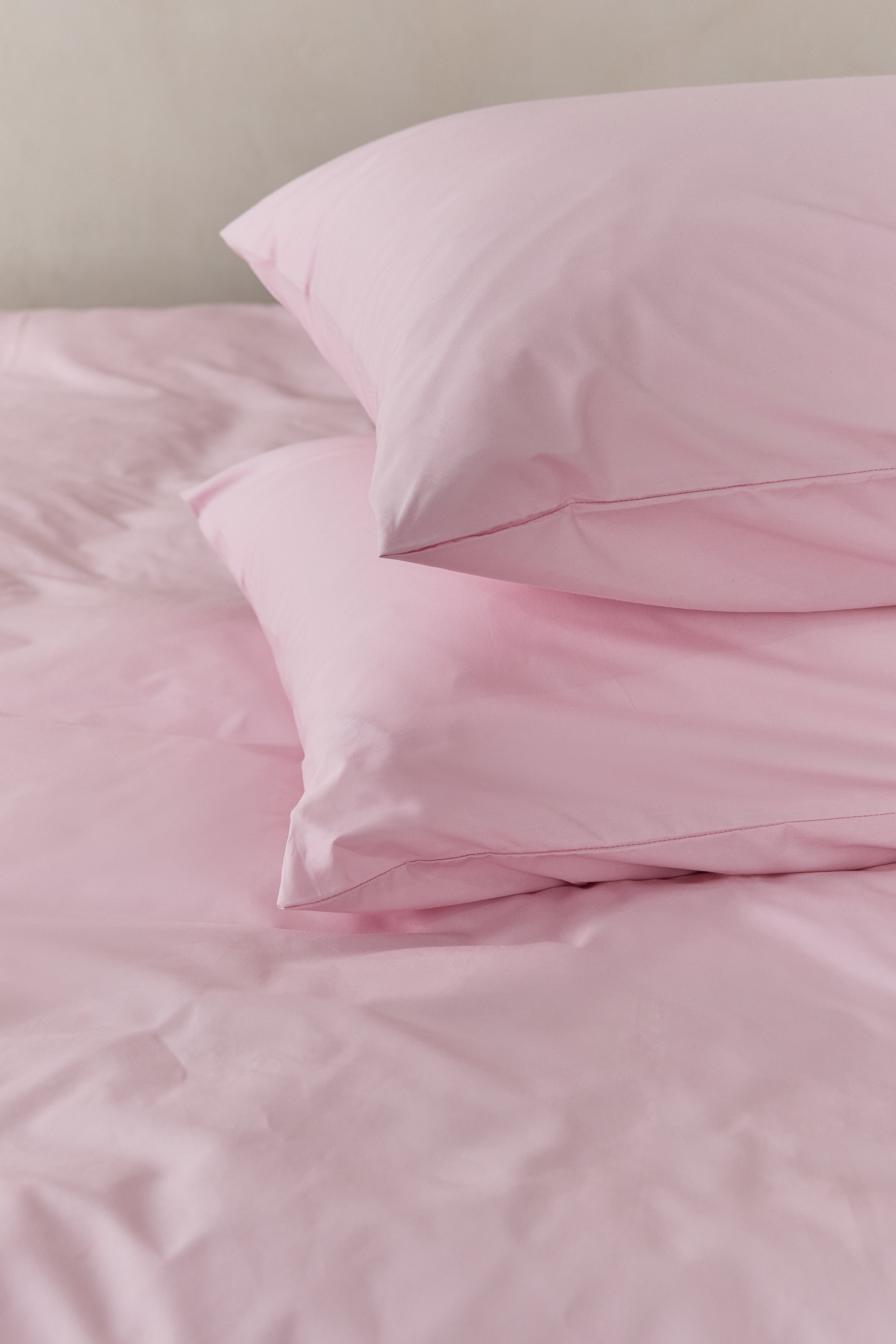 שתי כריות מונחות אחת על השניה עם ציפיות כותנה בצבע ורוד בהיר, על מיטה