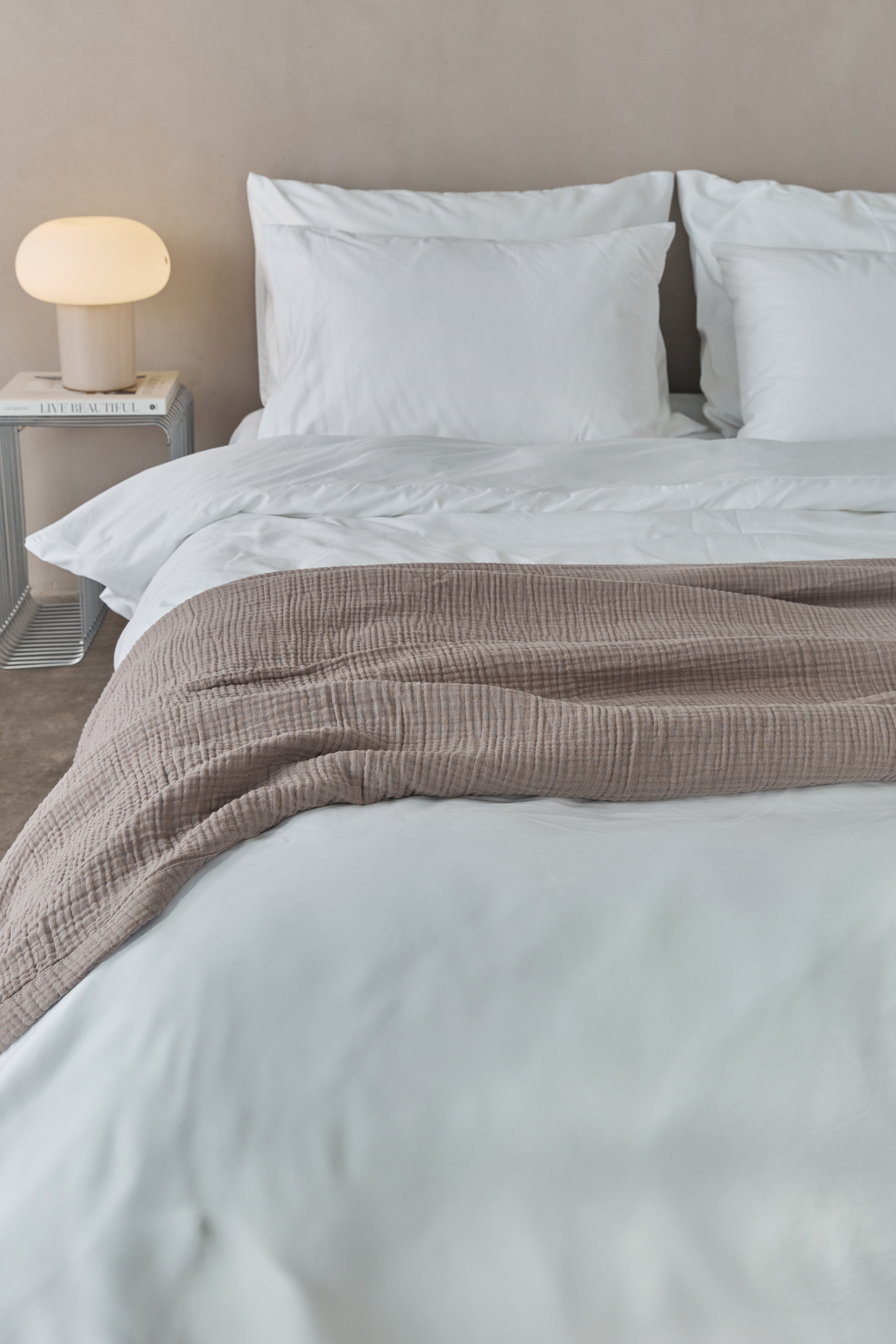 שמיכת מוסלין בצבע מוקה מונחת על מיטה זוגית עם מצעים לבנים