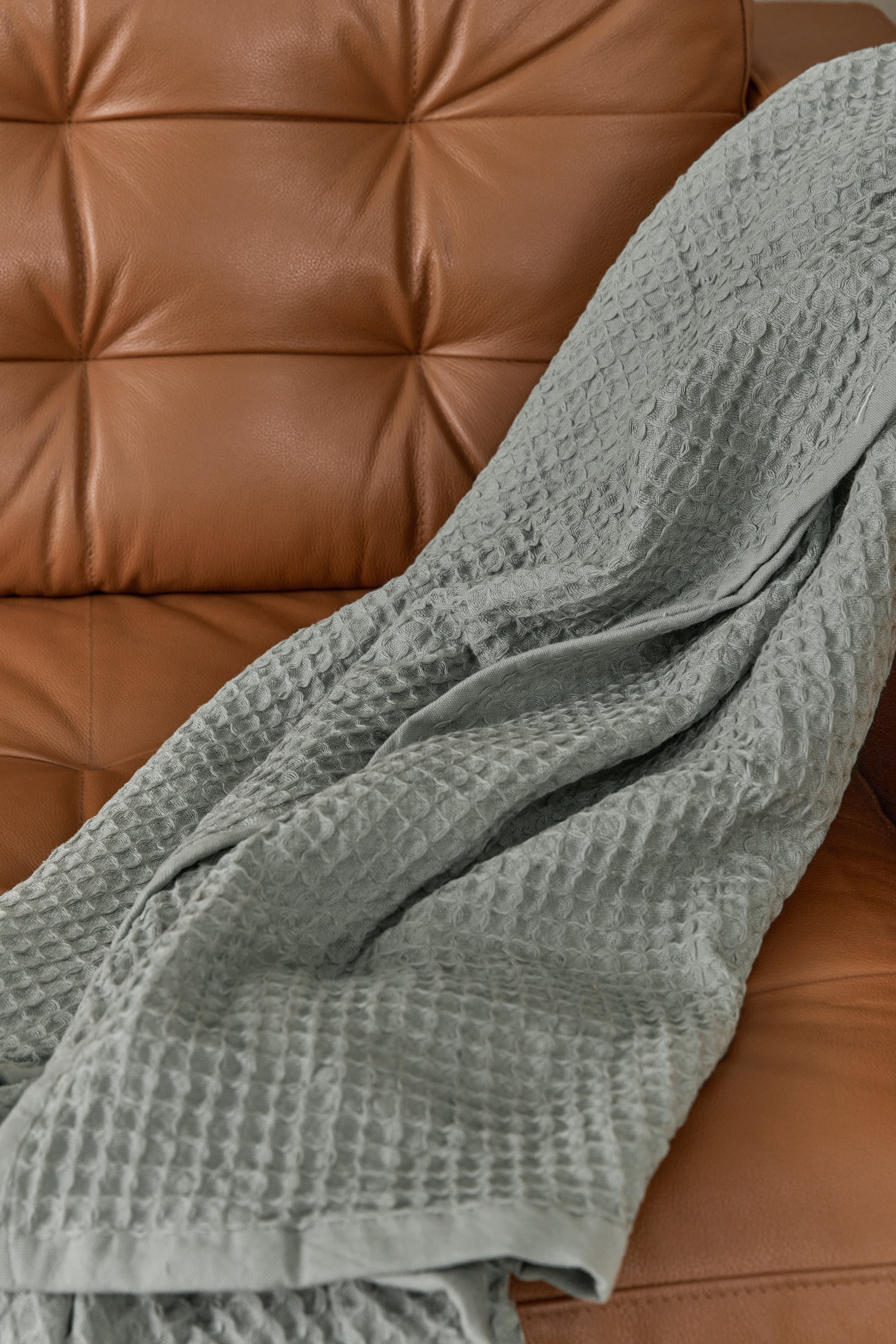 תקריב בד שמיכת פיקה בצבע ירוק מרווה מונחת על ספת עור חומה 