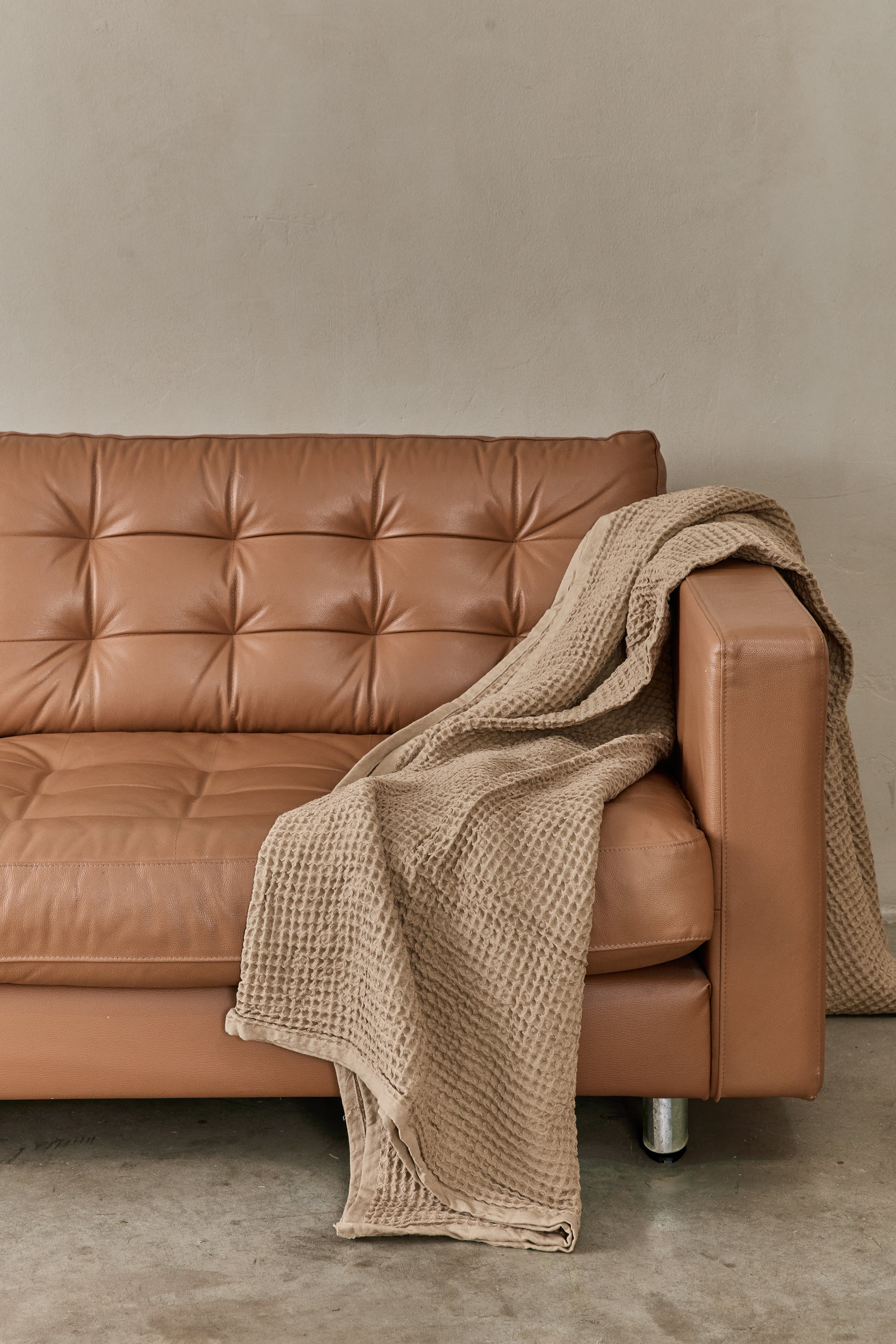 שמיכת פיקה בצבע מוקה מונחת על ספת עור בצבע חום 