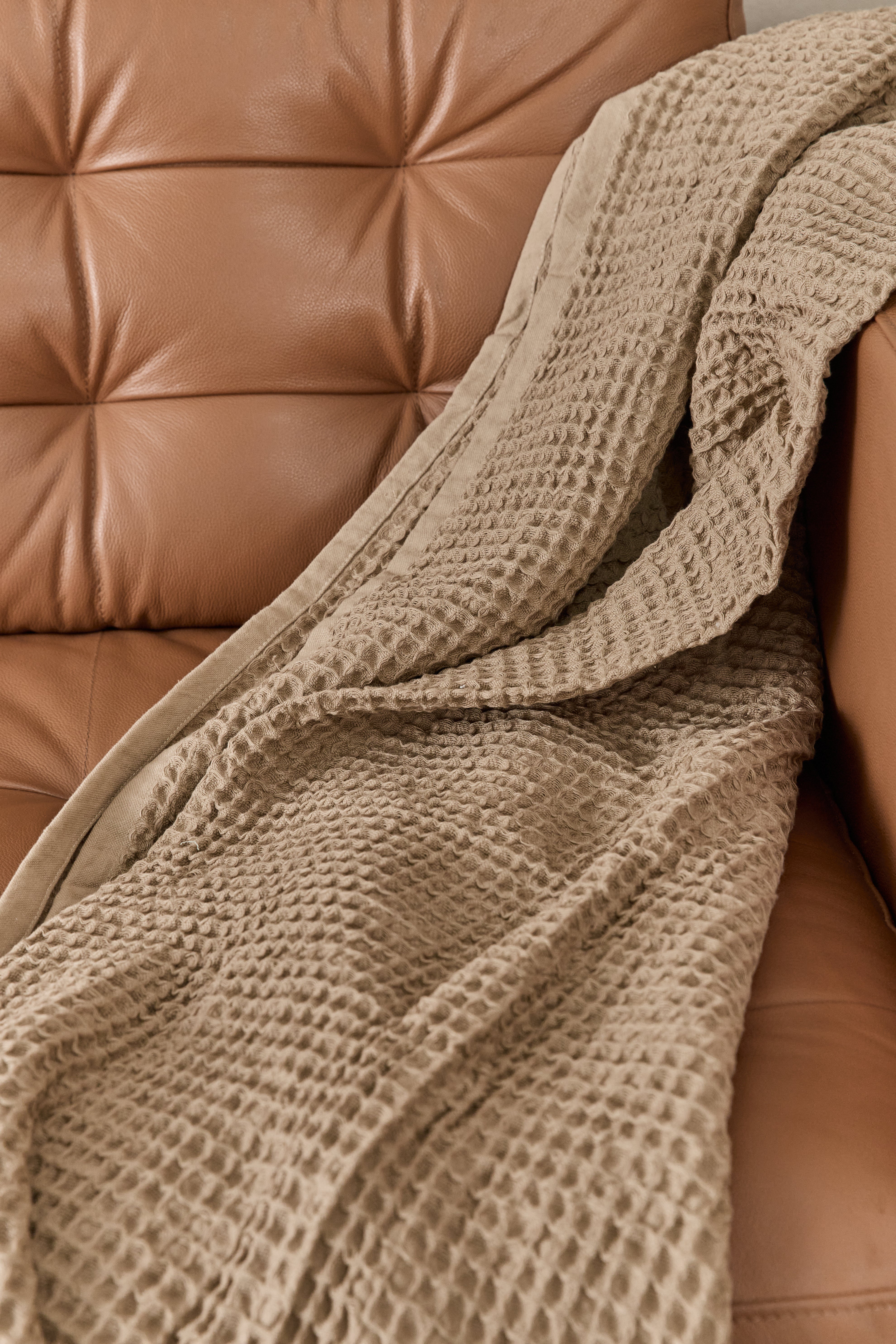 תקריב בד שמיכת פיקה בצבע מוקה זרוקה על ספת עור חומה 