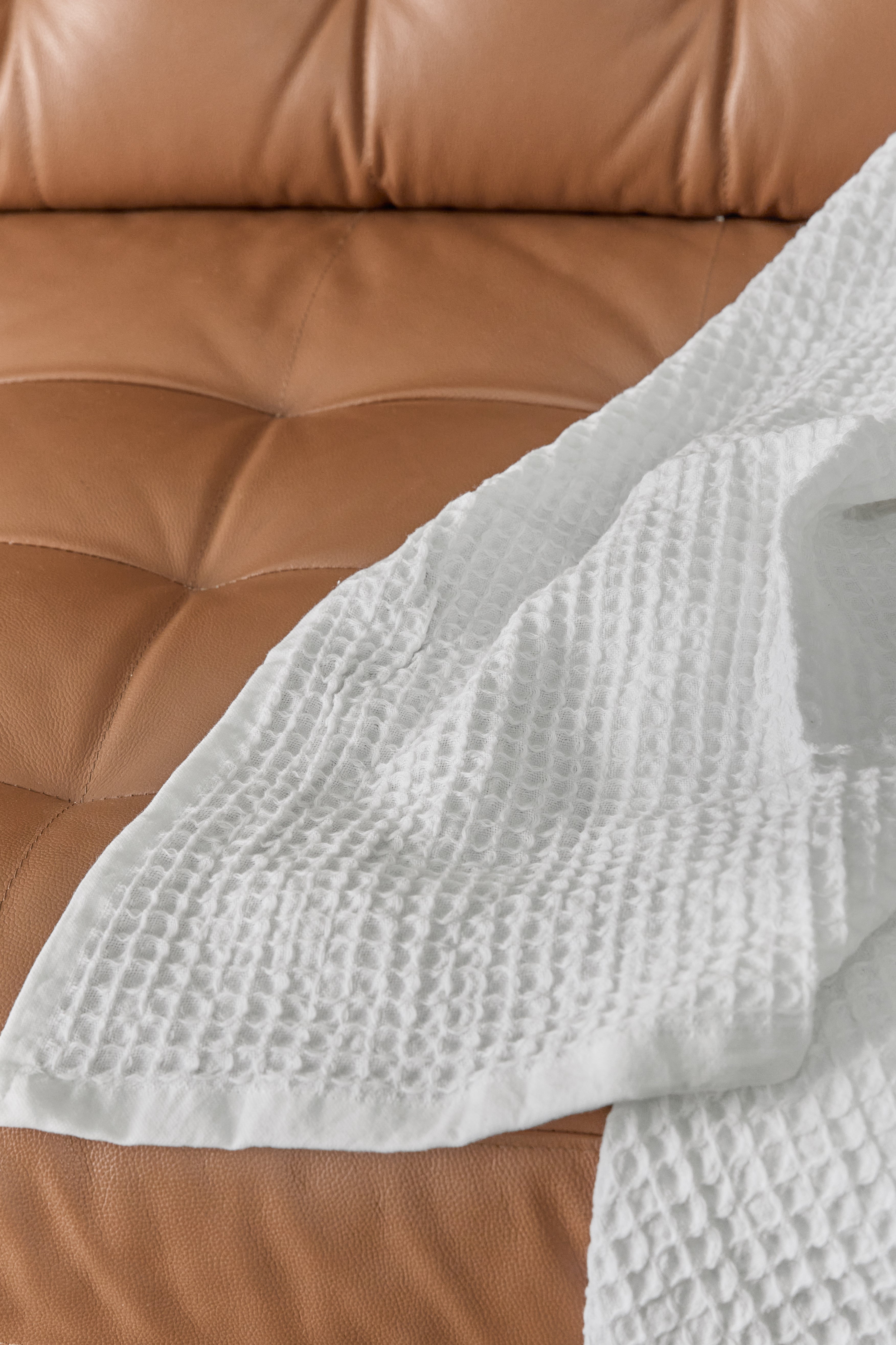 תקריב בד שמיכת פיקה לבנה זרוקה על ספת עור חומה