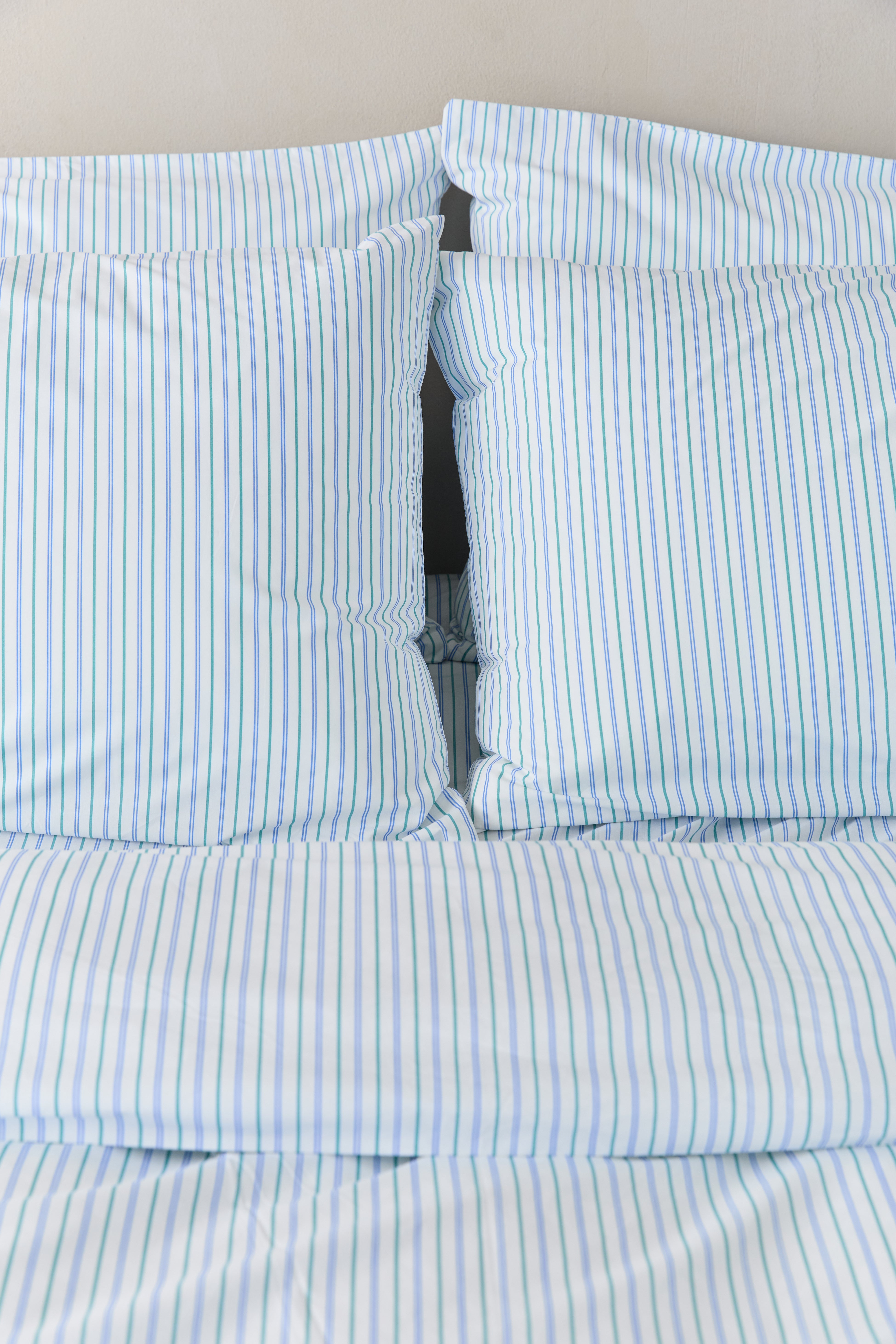 תקריב מיטה זוגית מצעי פרקל בצבע לבן עם פסים כחולים וירוקים