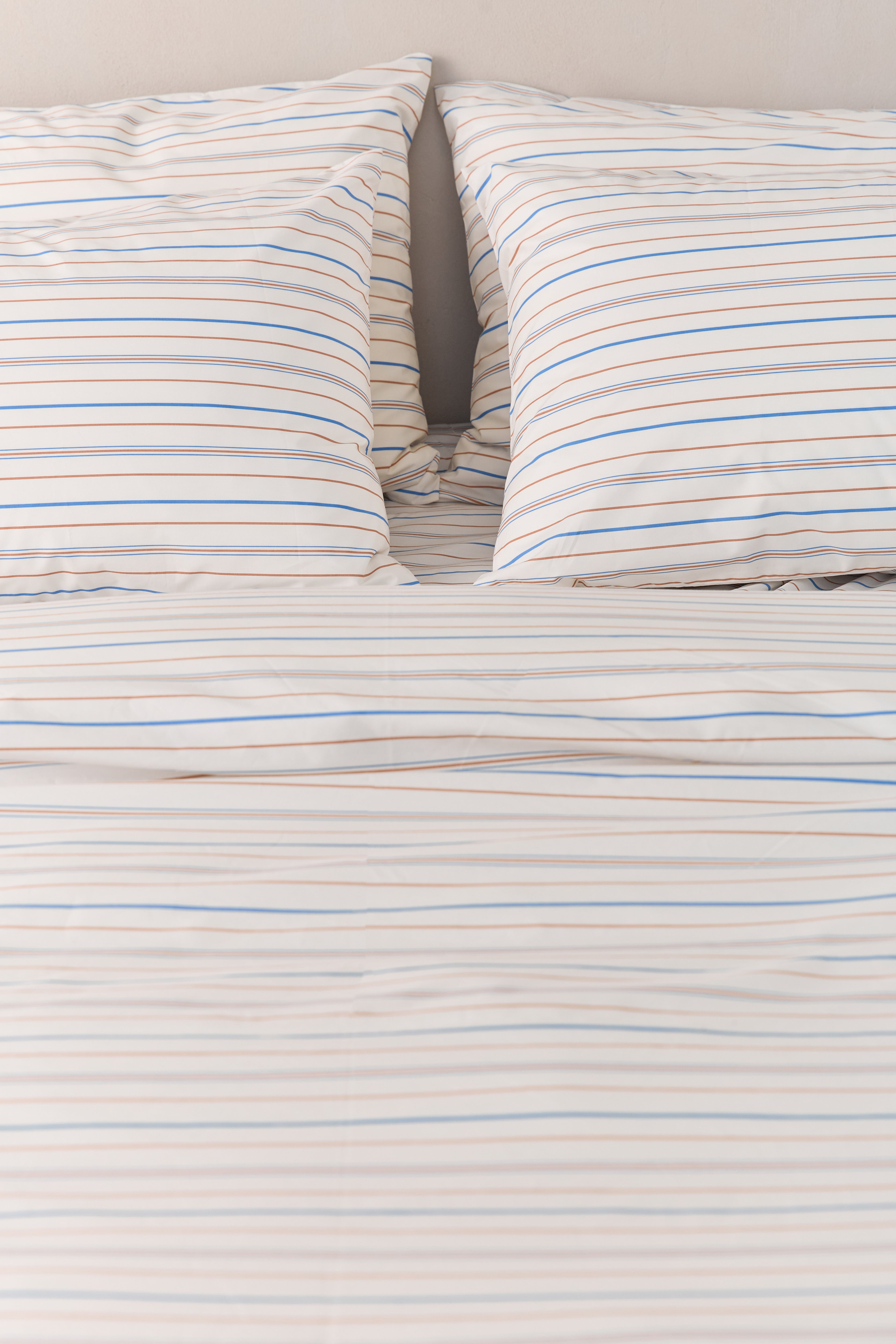 תקריב מיטה זוגית עם סט מצעי פרקל בצבע קרם עם פסים חומים וכחולים