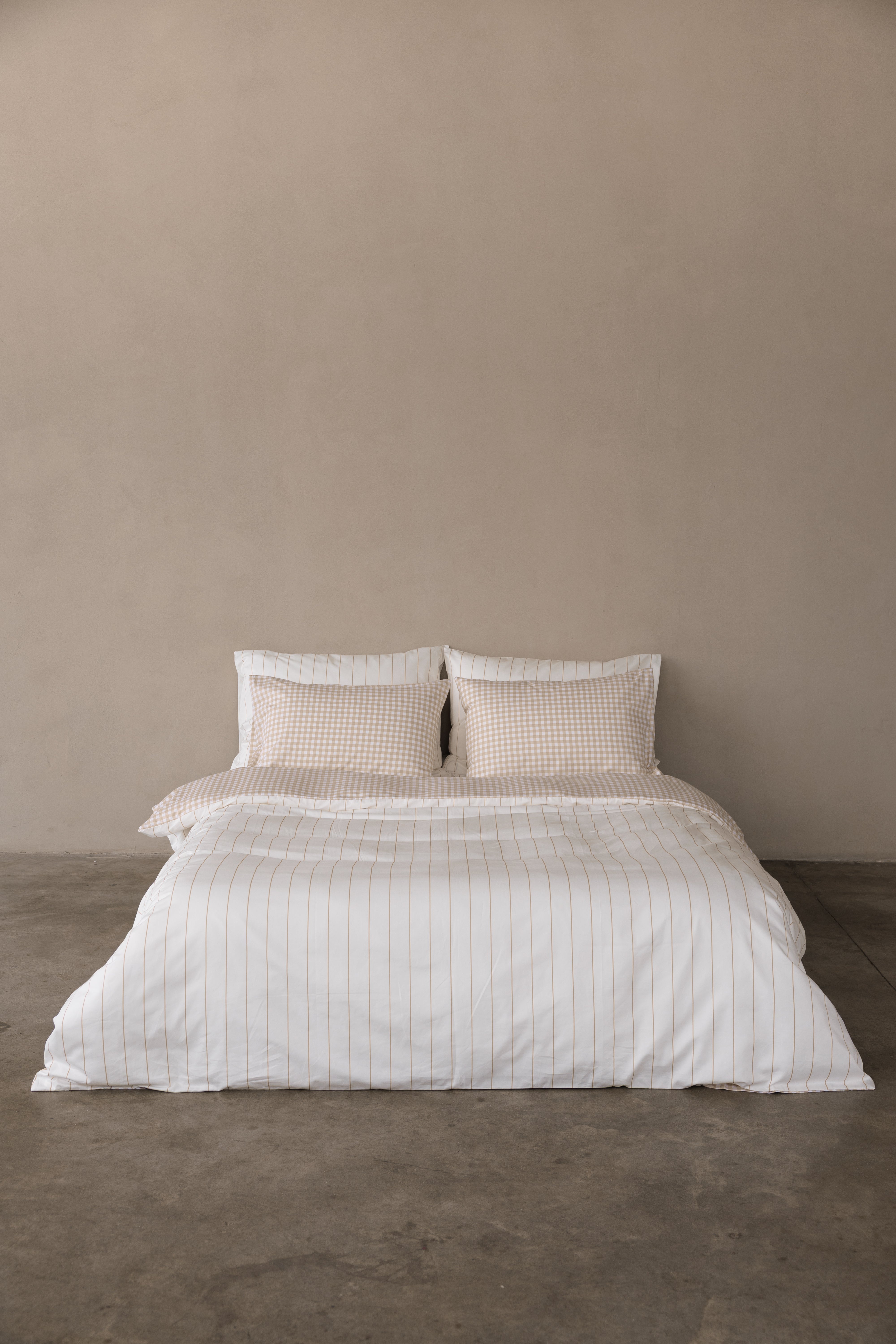 מיטה זוגית עם מצעי סאטן 500  כריות אחוריות לבנות עם פסים בז' וכריות קדמיות עם משבצות בצבע בז'. השמיכה דו צדדית צד אחד פסים צד אחד משבצות 