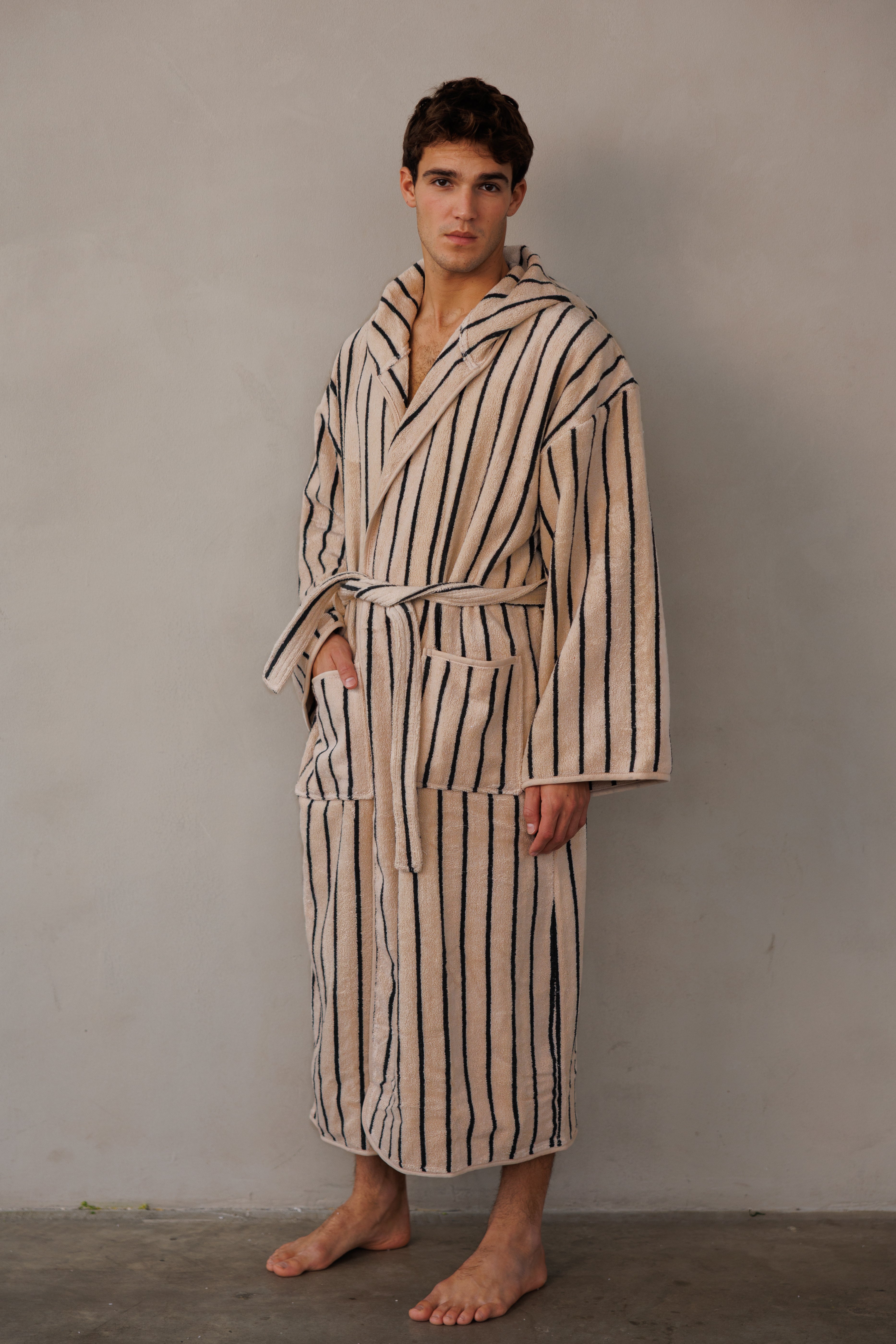 דוגמן עומד על הצד עם חלוק בצבע בז' עם פסים שחורים וידיים בכיסים 