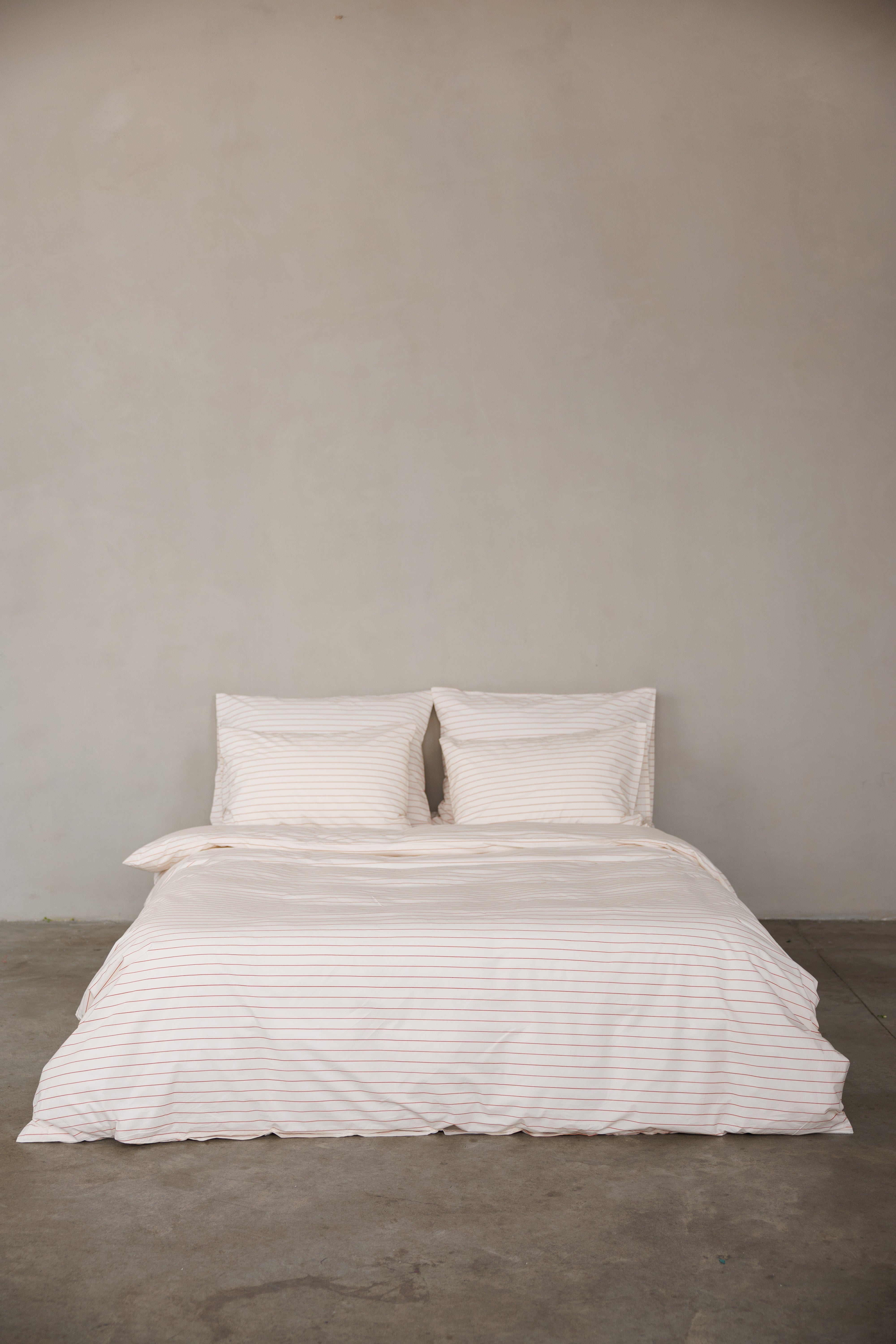 מיטה זוגית עם מצעי פרקל בצבע קרם עם פסים לרוחב בצבע אדום