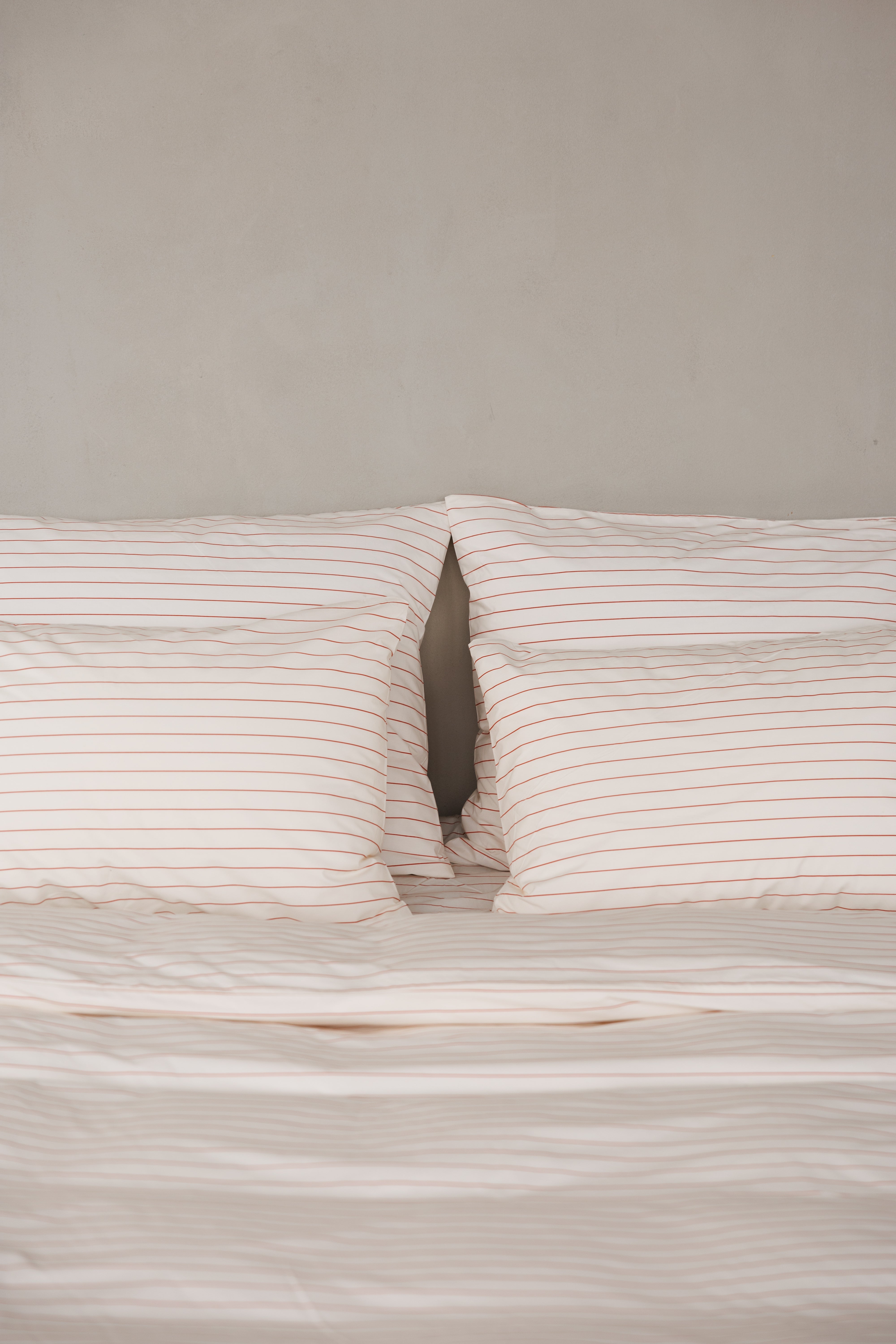 תקריב מיטה זוגית עם מצעי פרקל בצבע קרם עם פסים לרוחב בצבע אדום