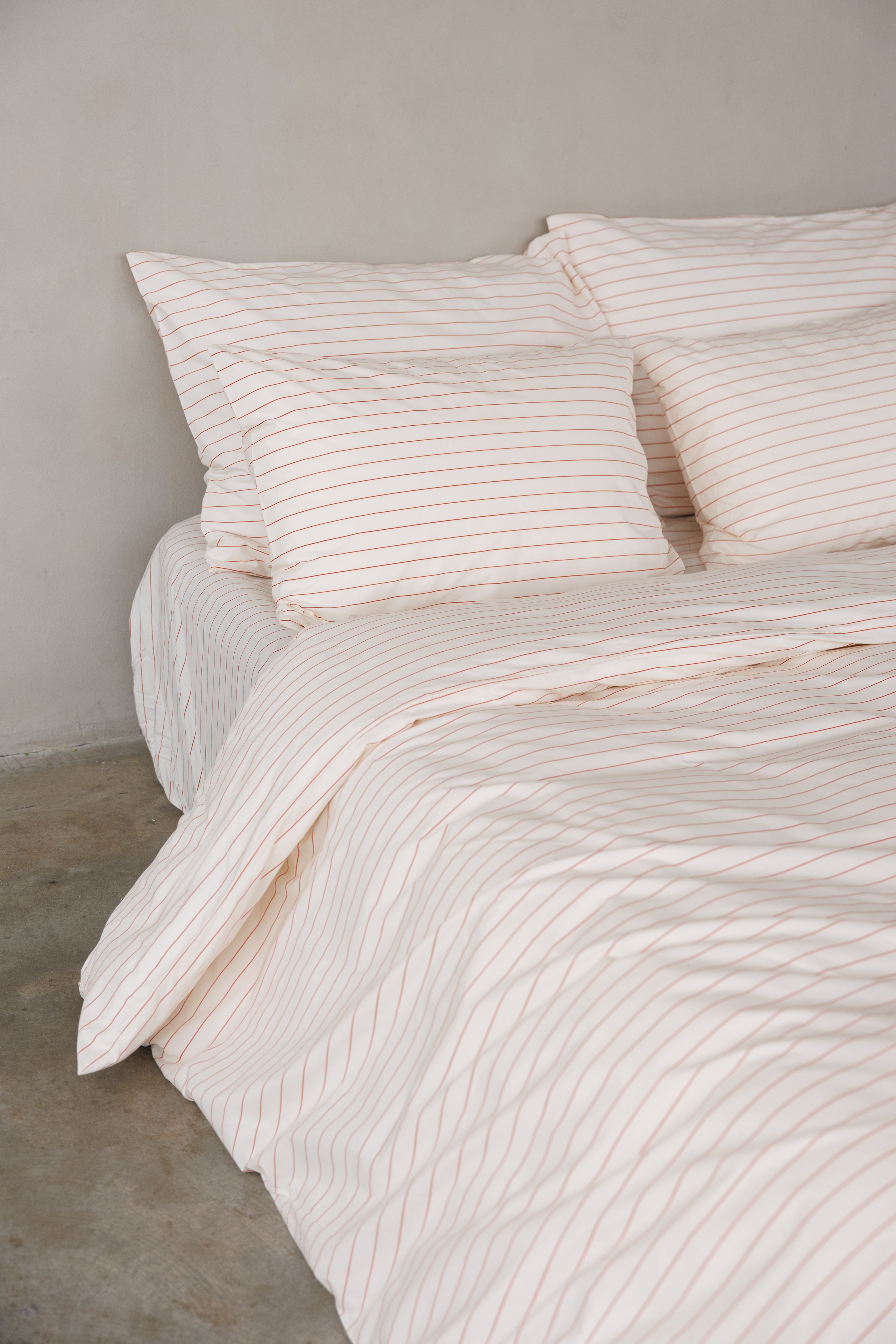 פינה של מיטה זוגית עם מצעי פרקל בצבע קרם עם פסים לרוחב בצבע אדום